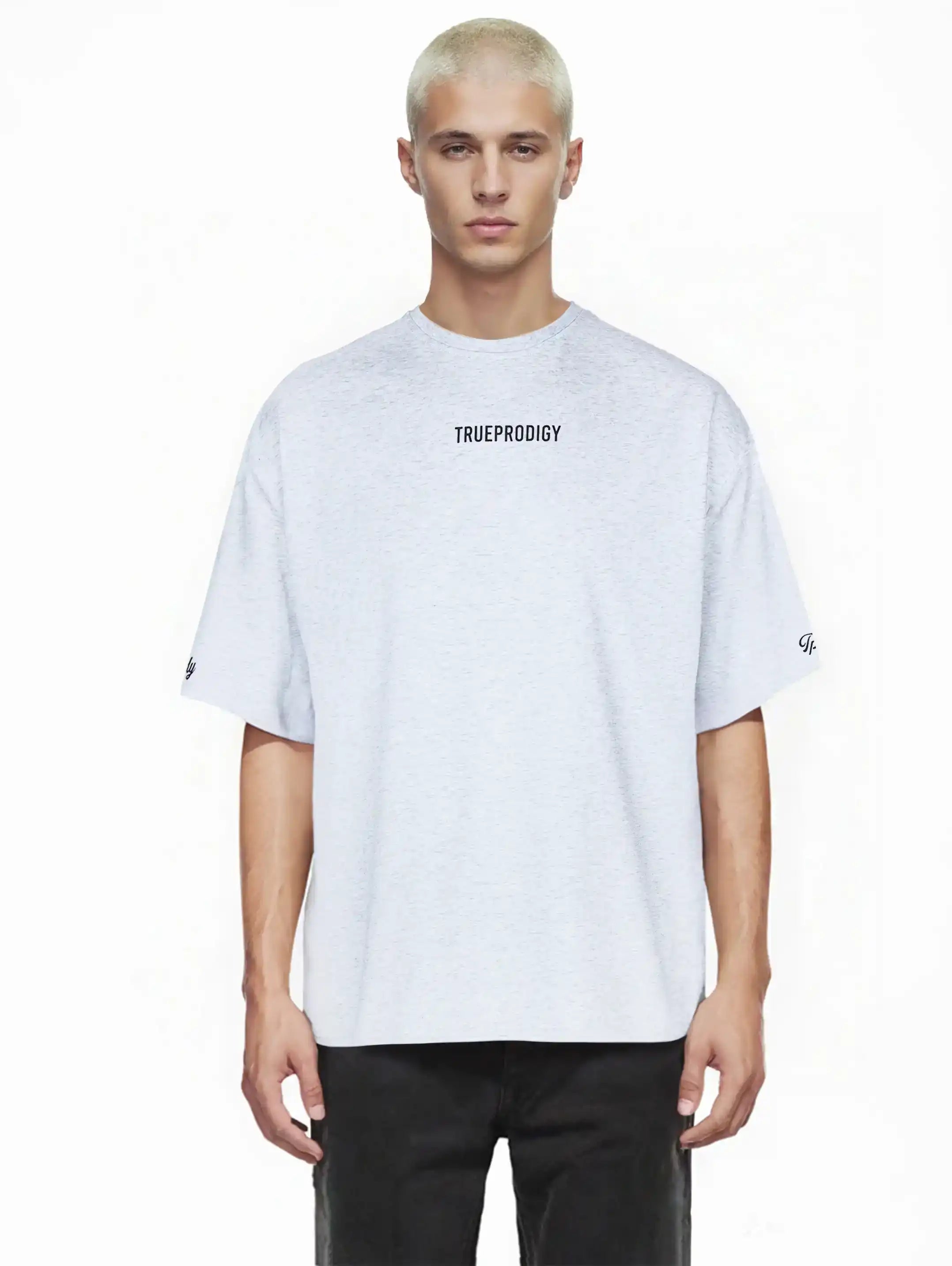 Ein junger Mann mit kurzen, gebleichten blonden Haaren blickt nach vorne in einem hellgrauen Kai Oversize-Herren-T-Shirt von trueprodigy mit Markenlogo vorne, Rückenprint "LIMITLESS" und schwarzen Hosen.
