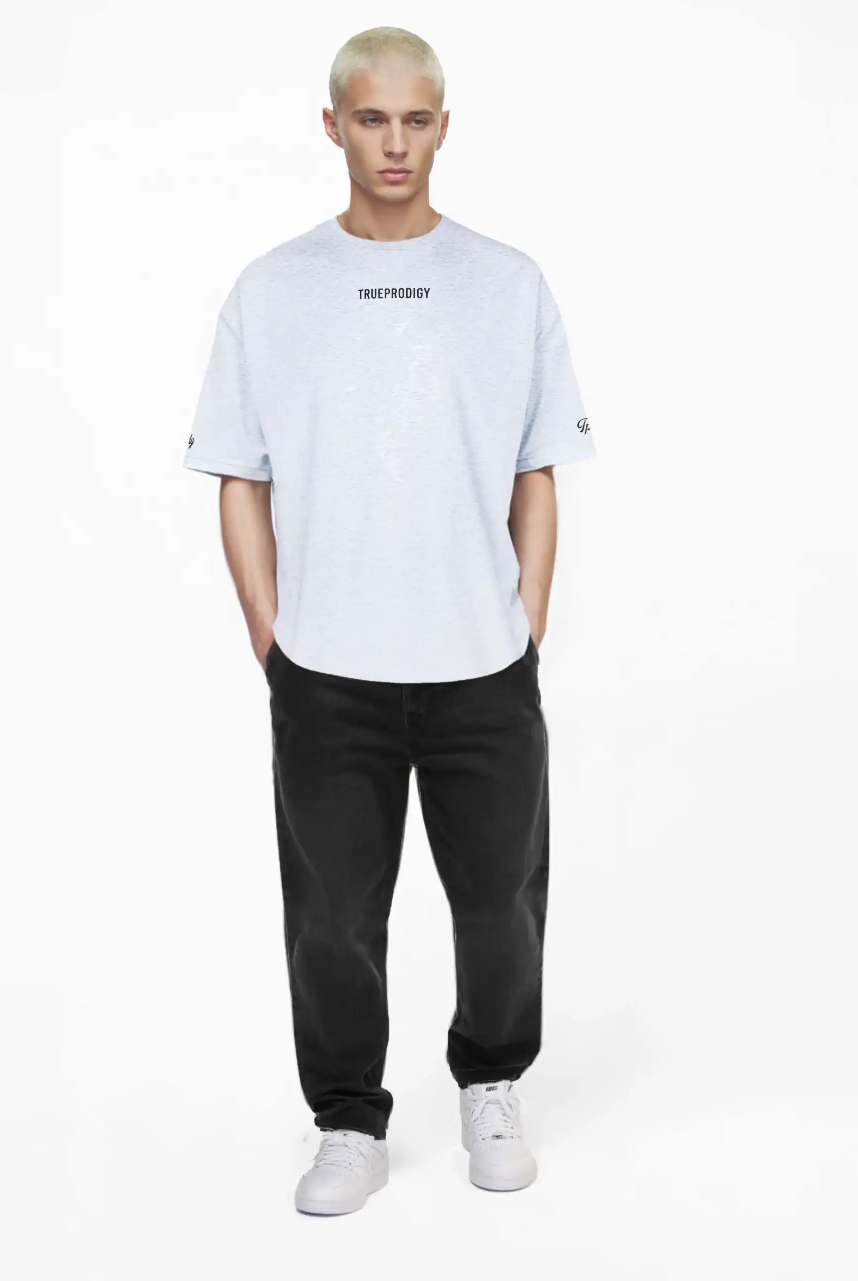 Eine Person mit kurzen, gebleachten blonden Haaren steht vor einem weißen Hintergrund und trägt das trueprodigy Kai Oversize-Herren-T-Shirt mit "LIMITLESS"-Rückenaufdruck und Logo auf der Vorderseite, gepaart mit einer schwarzen Jeans und weißen Sneakers.