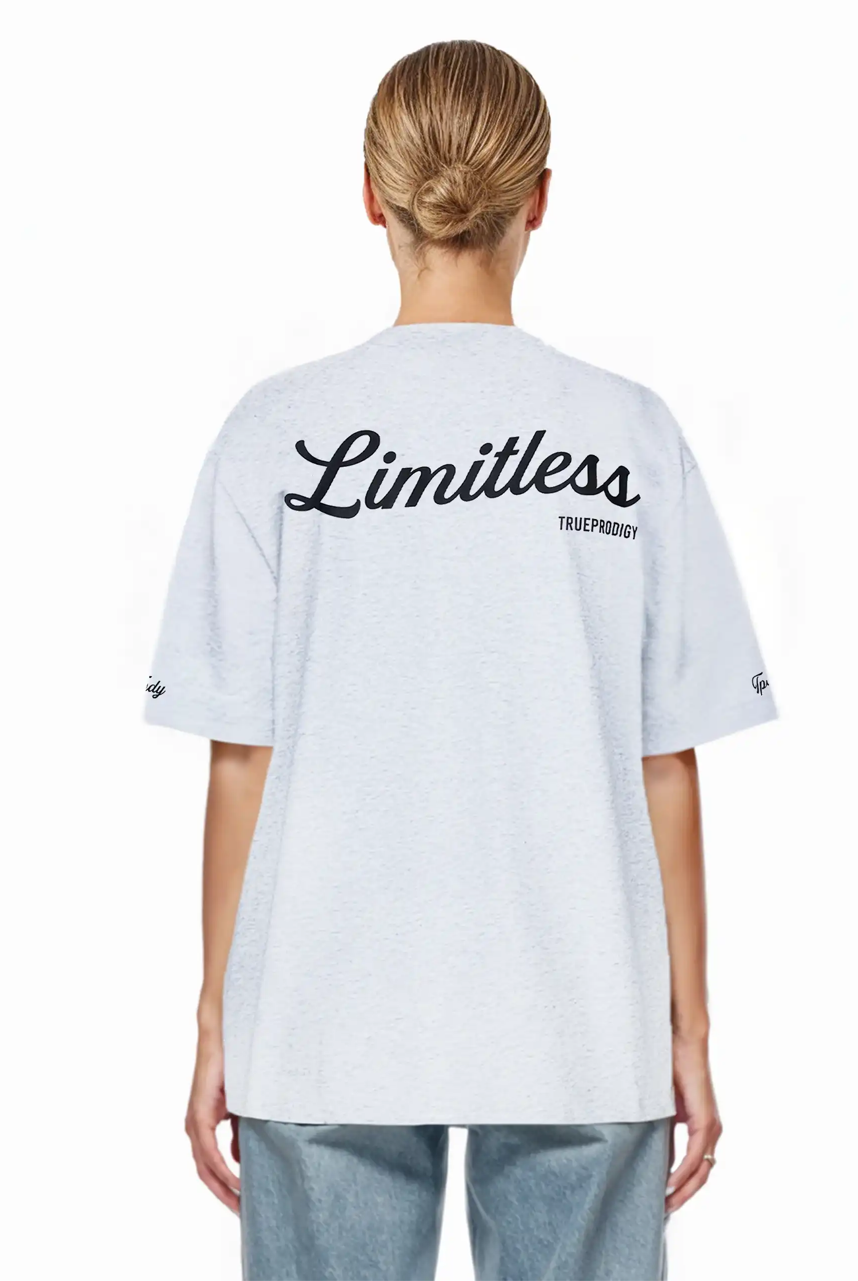 Eine blondhaarige Person mit tiefem Dutt trägt das trueprodigy Kai F Oversize-Damen-T-Shirt in Hellgrau mit dem Aufdruck "LIMITLESS" und dem Markennamen auf dem Rücken, von der Kamera abgewandt.