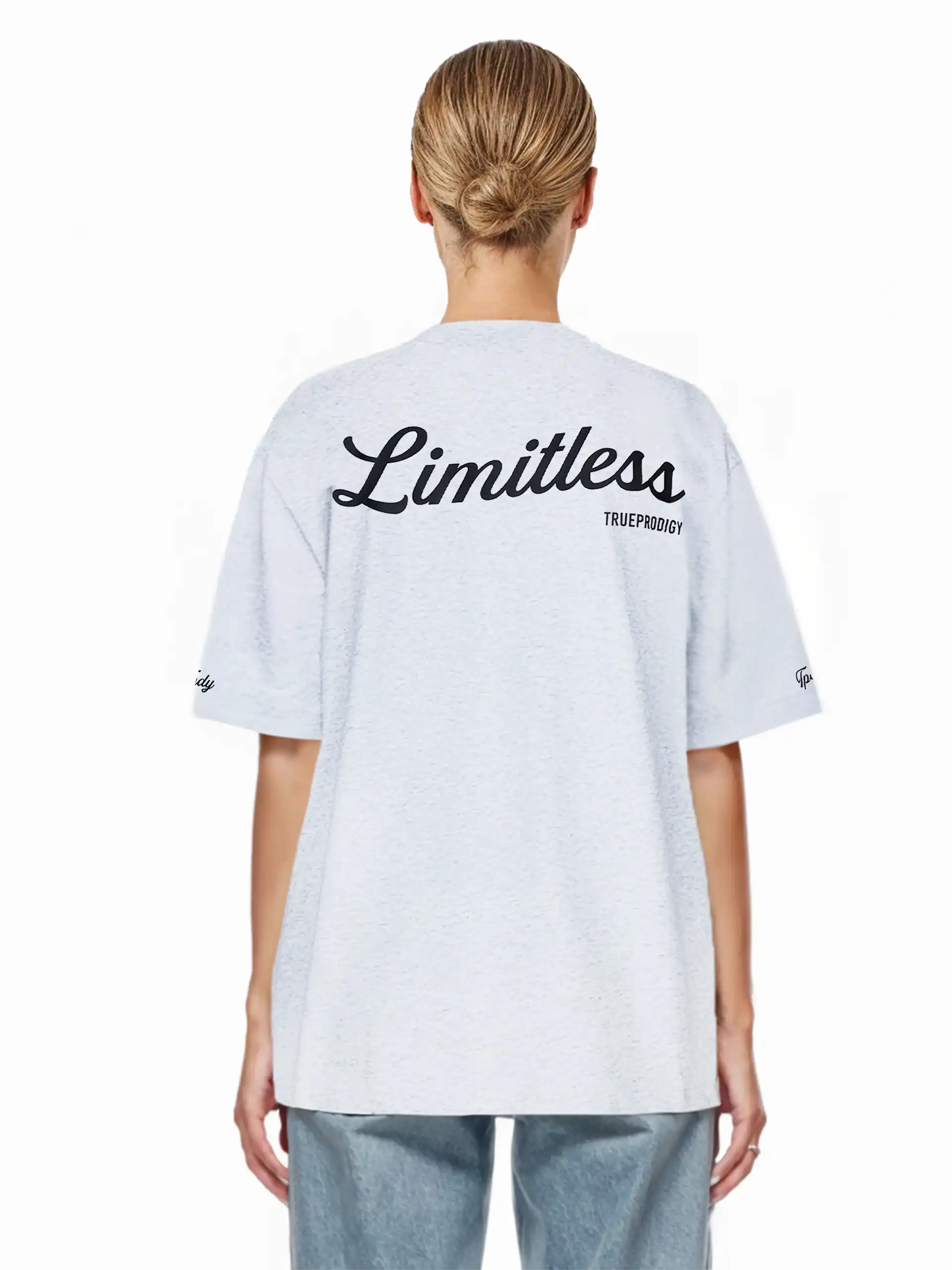 Eine blondhaarige Person mit tiefem Dutt trägt das trueprodigy Kai F Oversize-Damen-T-Shirt in Hellgrau mit dem Aufdruck "LIMITLESS" und dem Markennamen auf dem Rücken, von der Kamera abgewandt.