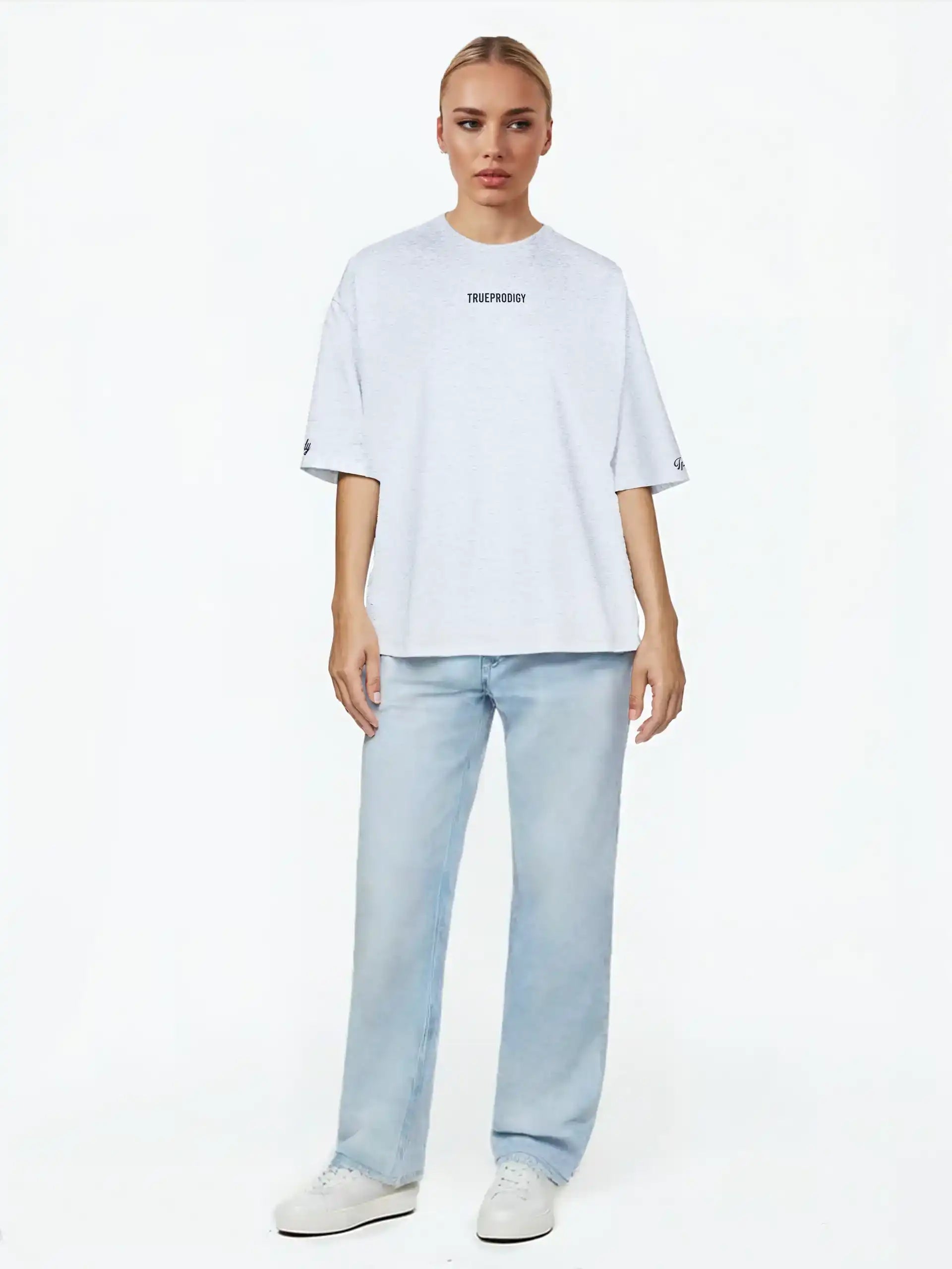 Eine Person blickt nach vorne und trägt das trueprodigy Kai F Oversize-Damen-T-Shirt mit Rückenprint "LIMITLESS", gepaart mit hellblauen Jeans und weißen Turnschuhen, vor einem schlichten weißen Hintergrund.