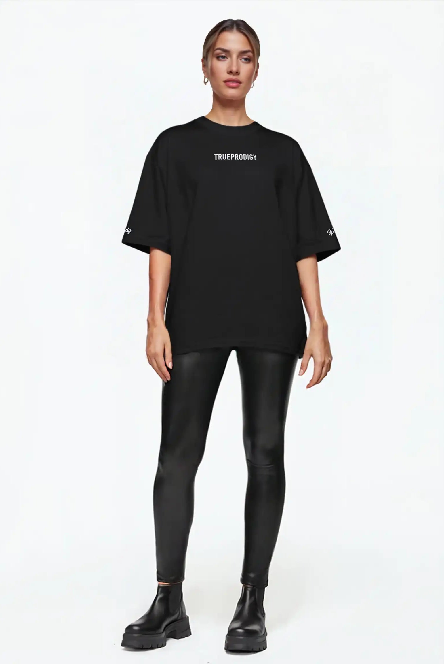 Eine Person blickt nach vorne in einem schwarzen trueprodigy Kai F Oversize-Damen-T-Shirt mit Rückenprint "LIMITLESS", gepaart mit schwarzen Leggings in Lederoptik und Ankle Boots, vor einem schlichten weißen Hintergrund.