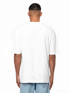 Eine Person steht von der Kamera abgewandt, trägt ein weißes Ravi Oversize-Shirt mit großem trueprodigy-Schriftzug vorn by trueprodigy und hellblaue Jeans vor weißem Hintergrund.