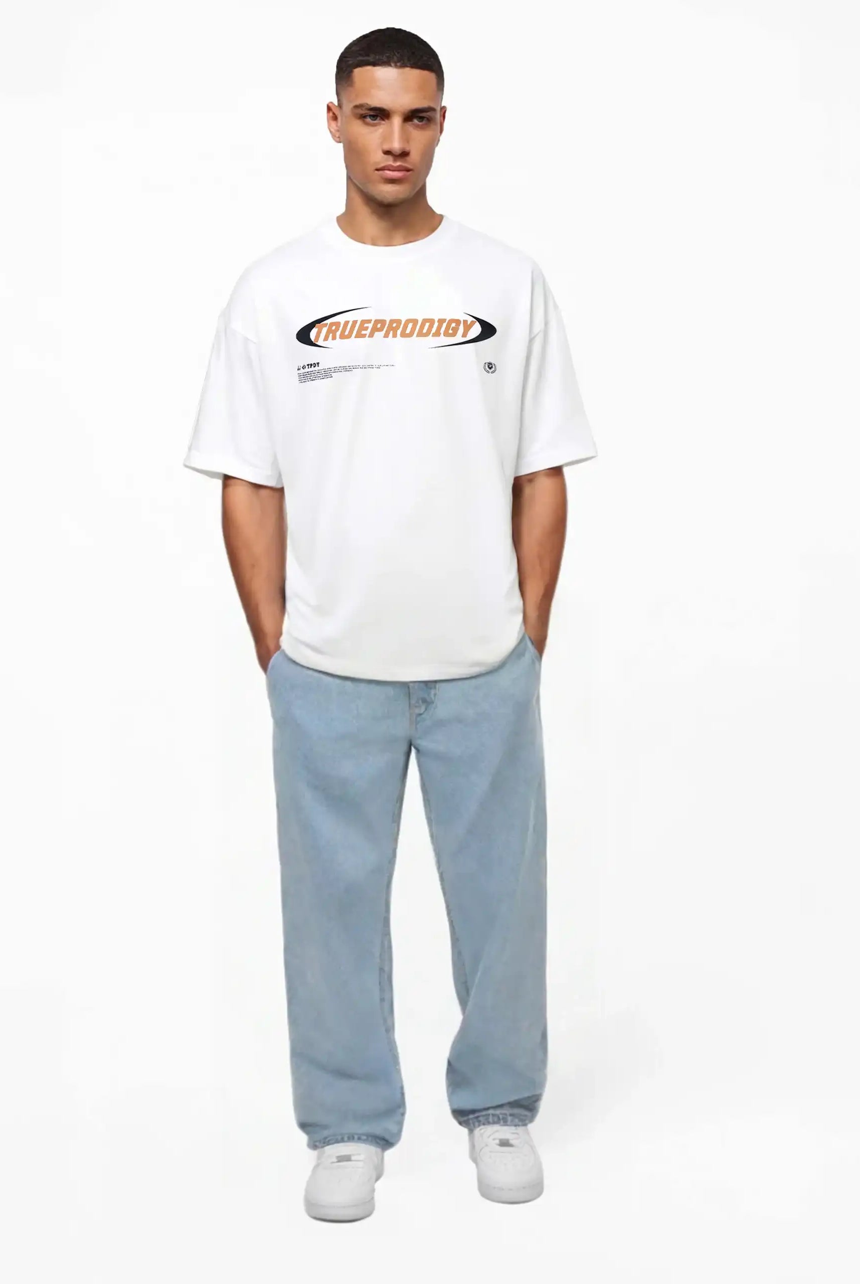 Ein Mann steht mit Blick nach vorne und trägt das trueprodigy Ravi Oversize-Shirt mit großem trueprodigy-Schriftzug vorn in weiß, gepaart mit hellblauen, locker sitzenden Jeans und weißen Turnschuhen. Der Hintergrund ist einfarbig weiß.