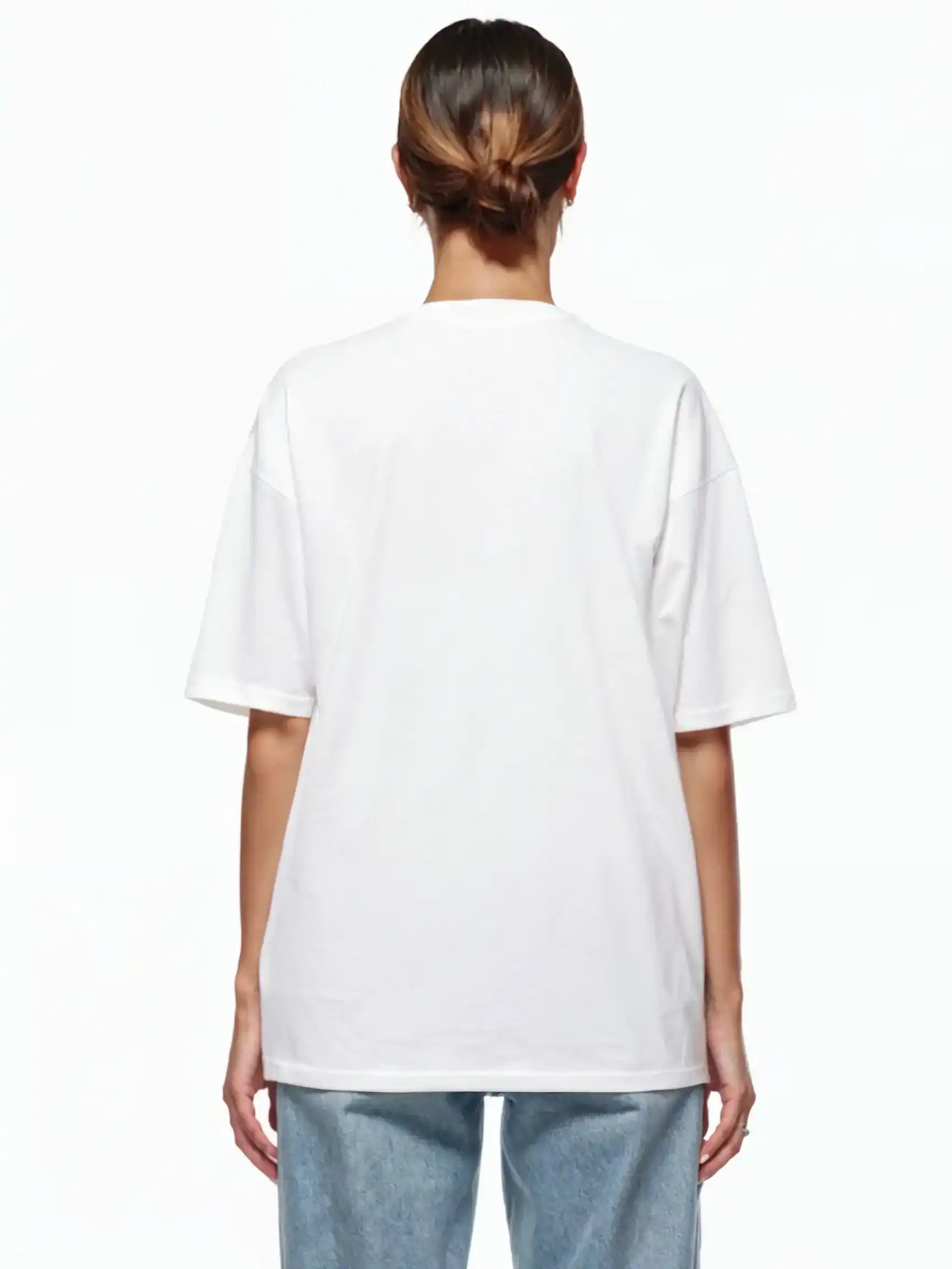 Gezeigt wird eine Person mit braunen Haaren in einem tiefen Dutt von hinten, die ein trueprodigy Ravi F Oversize-T-Shirt mit farbigem TRUEPRODIGY-Frontprint und hellblaue Jeans vor einem weißen Hintergrund trägt.