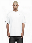 Eine Person mit kurzen, hellblonden Haaren trägt das trueprodigy Marin Oversize-T-Shirt mit edlem Schriftzug auf der Brust in schlichtem Weiß mit kleiner schwarzer Schrift, gepaart mit einer schwarzen Hose, vor einem weißen Hintergrund.