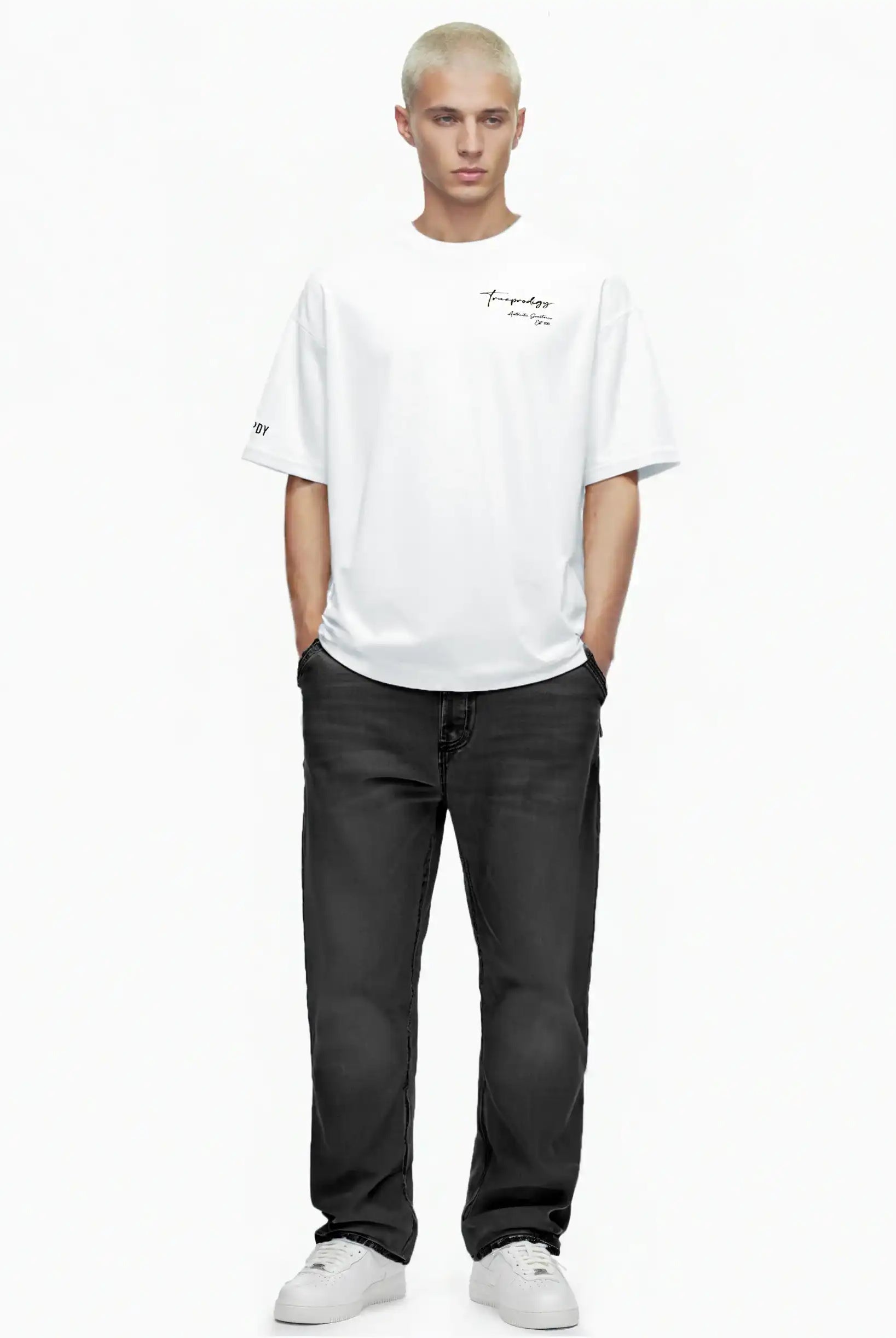 Eine Person mit kurzen blonden Haaren steht mit dem Gesicht nach vorne, trägt das trueprodigy Marin Oversize-T-Shirt mit edlem Schriftzug auf der Brust, schwarze Jeans und weiße Turnschuhe auf einem schlichten weißen Hintergrund. Die Hände sind in den Taschen.