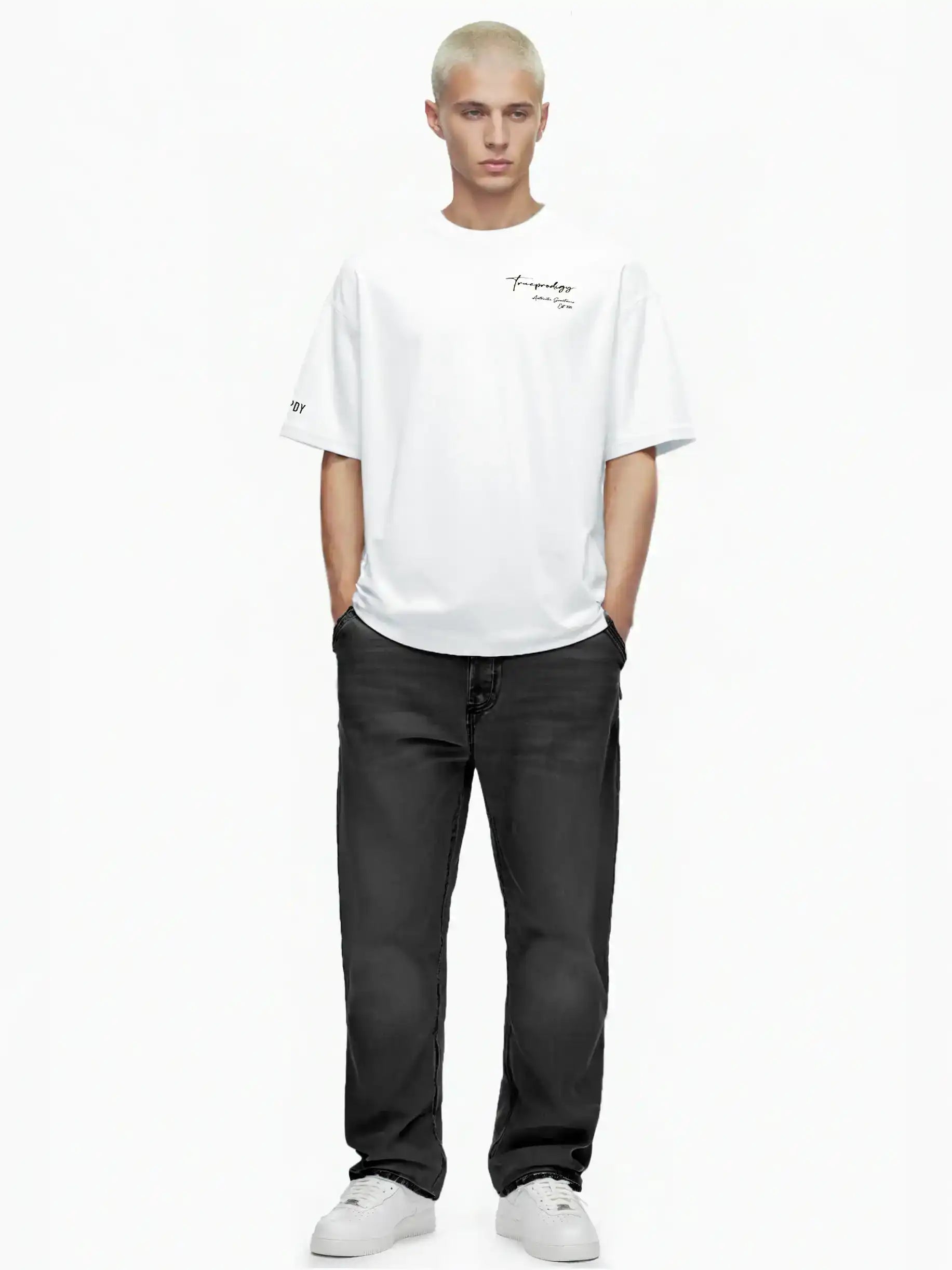 Eine Person mit kurzen blonden Haaren steht mit dem Gesicht nach vorne, trägt das trueprodigy Marin Oversize-T-Shirt mit edlem Schriftzug auf der Brust, schwarze Jeans und weiße Turnschuhe auf einem schlichten weißen Hintergrund. Die Hände sind in den Taschen.