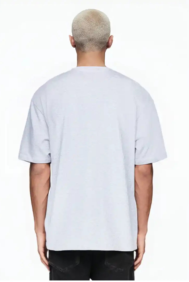 Eine Person mit kurzen, gebleichten blonden Haaren steht mit dem Rücken zur Kamera und trägt das trueprodigy Marin Oversize-T-Shirt mit edlem Schriftzug auf der Brust in hellgrau und schwarzer Hose vor einem schlichten weißen Hintergrund.