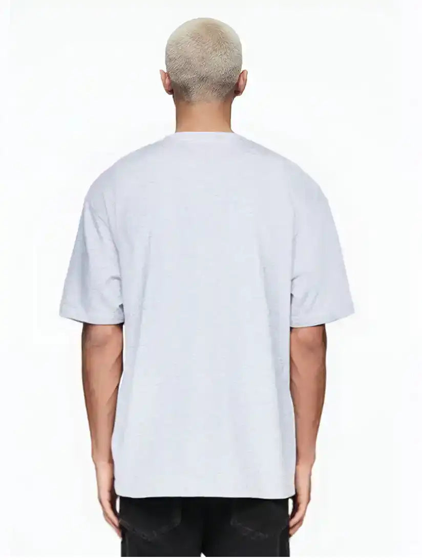 Eine Person mit kurzen, gebleichten blonden Haaren steht mit dem Rücken zur Kamera und trägt das trueprodigy Marin Oversize-T-Shirt mit edlem Schriftzug auf der Brust in hellgrau und schwarzer Hose vor einem schlichten weißen Hintergrund.