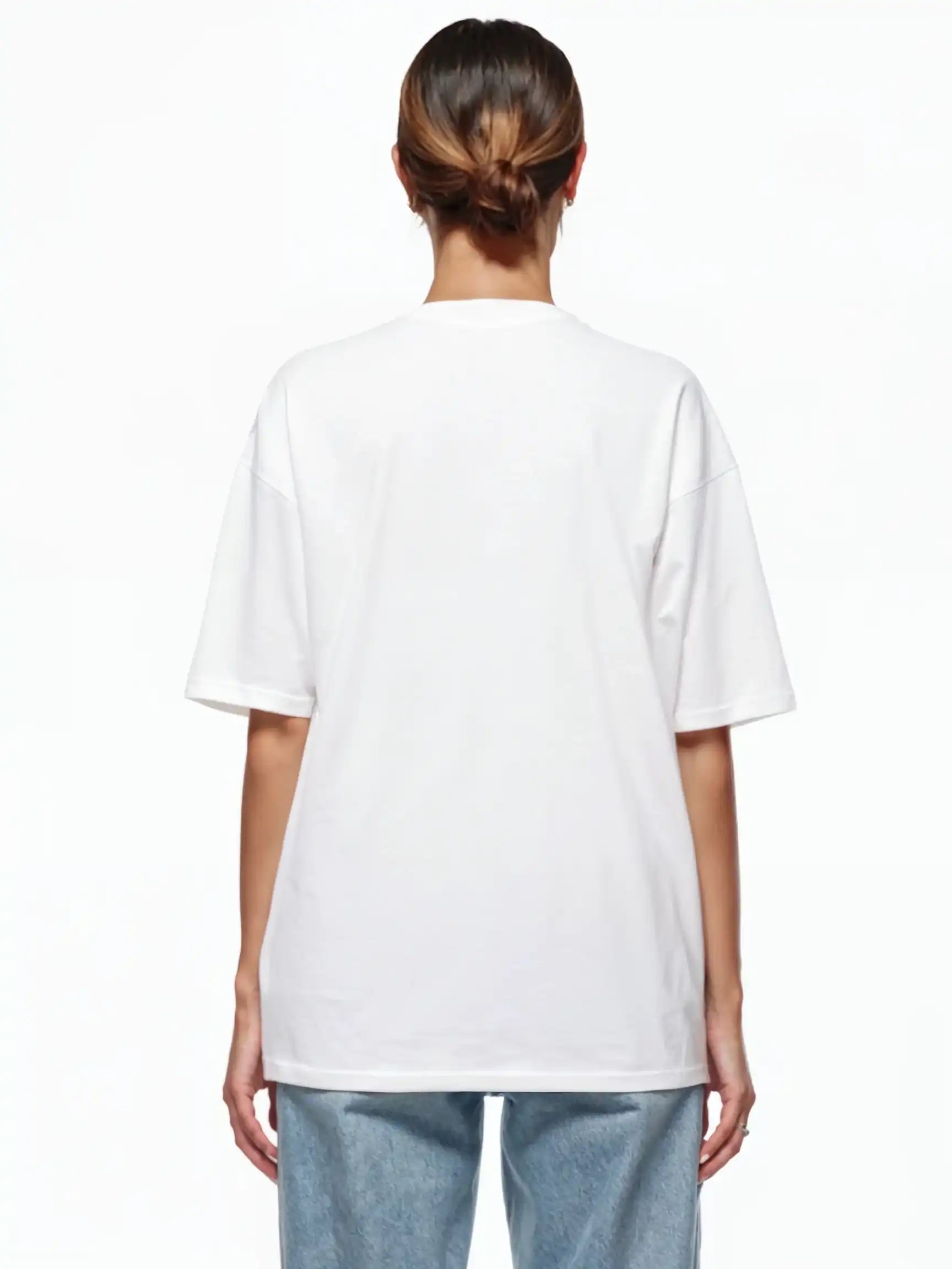 Gezeigt wird eine Person mit zurückgebundenem Haar von hinten, die ein schlichtes weißes trueprodigy Marin F Oversize-T-Shirt mit feiner Logo-Schrift & TPDY-Print am Ärmel und hellblaue Jeans vor weißem Hintergrund trägt.