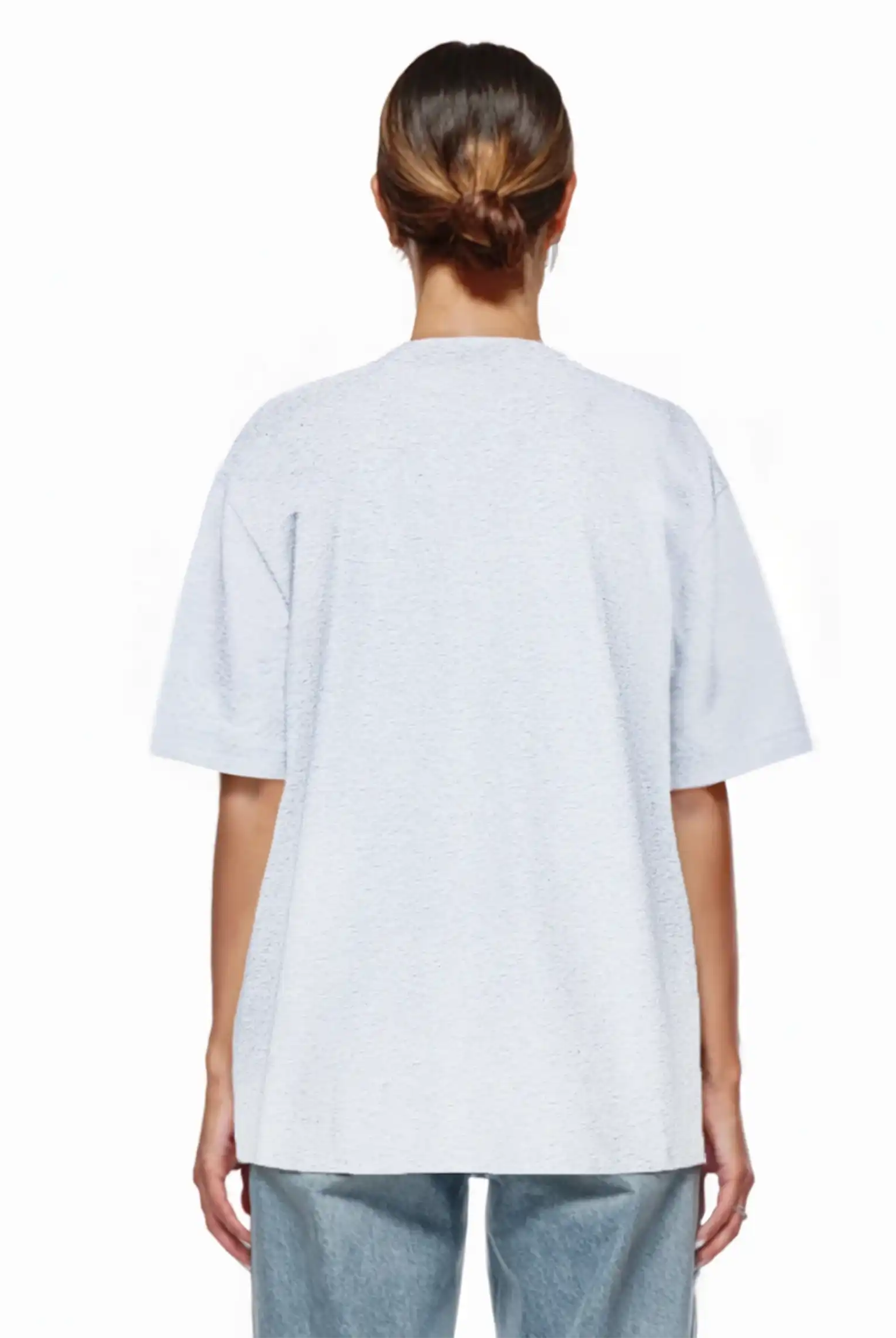 Eine Person mit braunen Haaren in einem tiefen Dutt ist von hinten zu sehen. Sie trägt das trueprodigy Marin F Oversize-T-Shirt mit feiner Logo-Schrift & TPDY-Print am Ärmel und hellblaue Jeans, unisex gestylt, vor einem schlichten weißen Hintergrund.