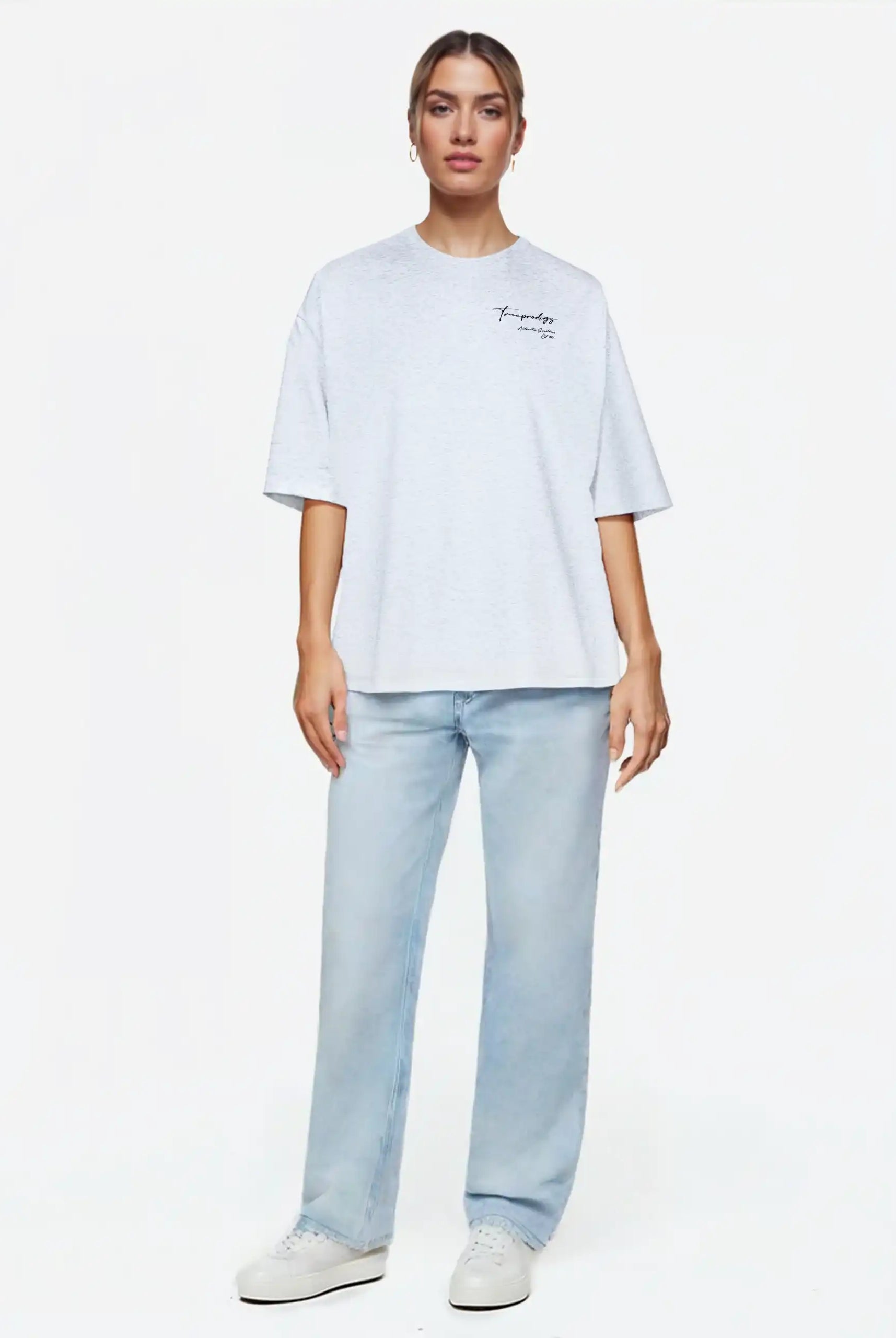 Eine Person schaut nach vorne und trägt ein hellgraues trueprodigy Marin F Oversize-T-Shirt mit feiner Logo-Schrift & TPDY-Print am Ärmel, gepaart mit hellblauen Jeans und weißen Turnschuhen, vor einem schlichten weißen Hintergrund.