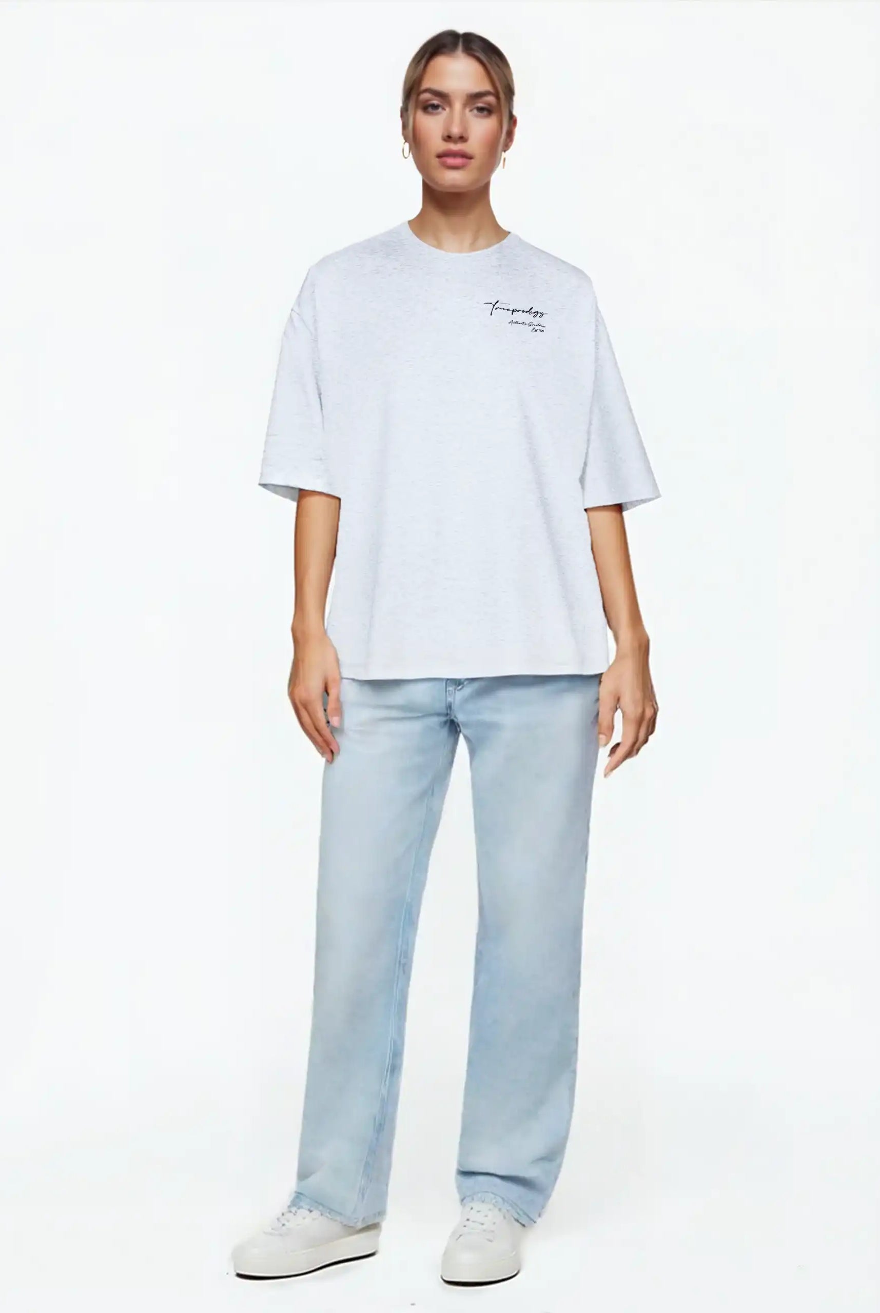 Eine Person blickt nach vorne in einem trueprodigy Marin F Oversize-T-Shirt mit feiner Logo-Schrift & TPDY-Print am Ärmel (hellgrau, unisex), gepaart mit hellblauen Jeans und weißen Turnschuhen vor einem schlichten weißen Hintergrund.
