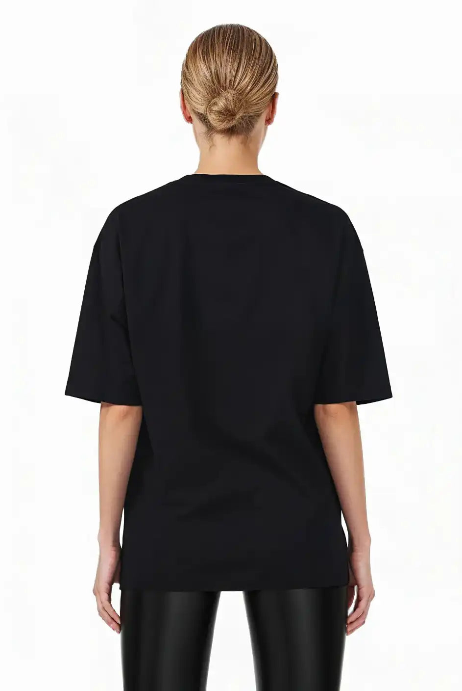 Eine Person mit blonden Haaren in einem tiefen Dutt steht mit dem Blick abgewandt, trägt das trueprodigy Marin F Oversize-T-Shirt mit feiner Logo-Schrift & TPDY-Print am Ärmel und eine glänzende schwarze Hose vor einem schlichten weißen Hintergrund.