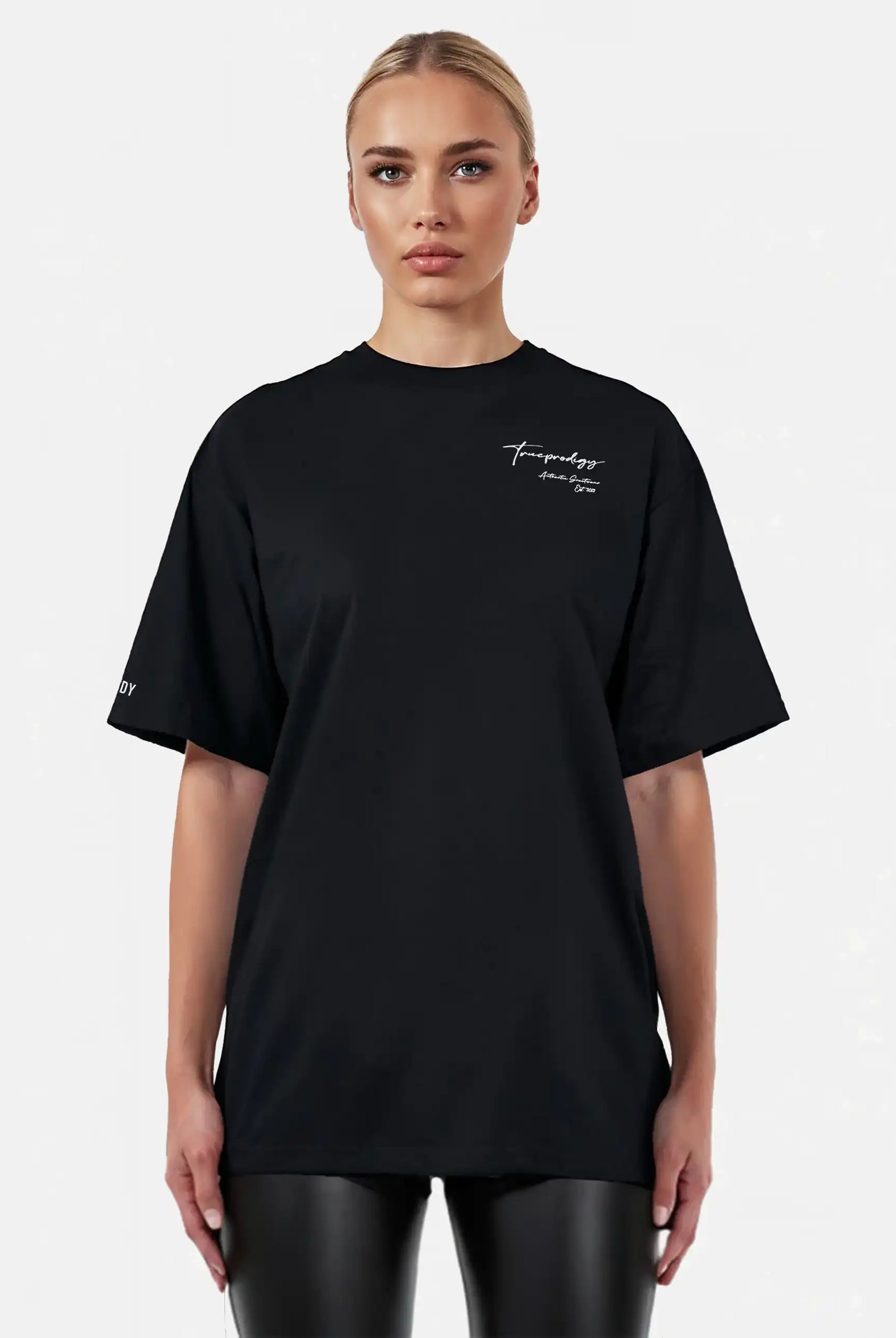 Eine Person blickt nach vorne in einem lockeren, unisex trueprodigy Marin F Oversize-T-Shirt mit feiner Logo-Schrift & TPDY-Print am Ärmel in Schwarz, gepaart mit einer schwarzen Lederhose, vor einem schlichten hellen Hintergrund.