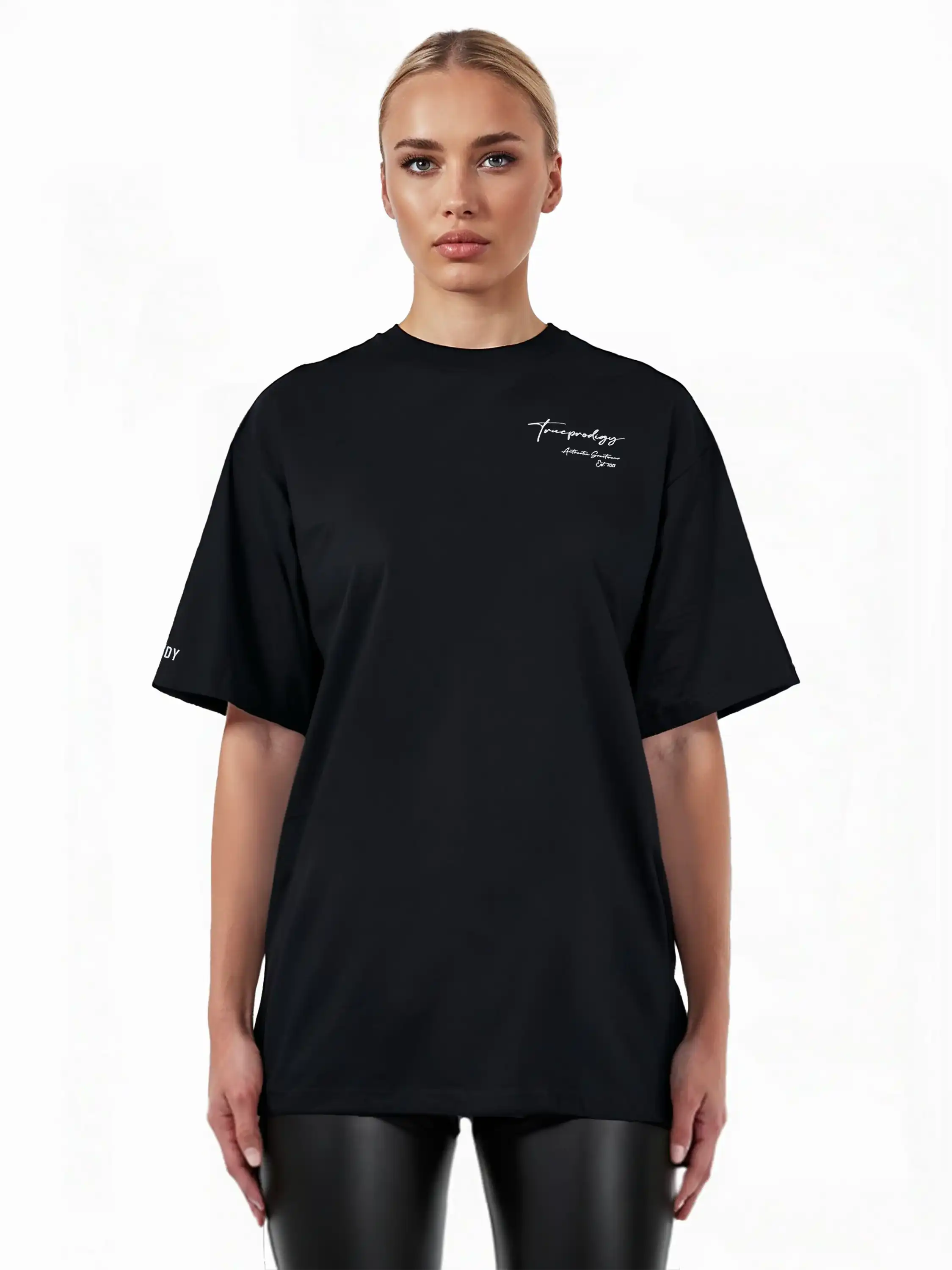 Eine Person mit zurückgesteckten blonden Haaren trägt das trueprodigy Marin F Oversize-T-Shirt mit feiner Logo-Schrift & TPDY-Print am Ärmel, gepaart mit einer schwarzen Kunstlederhose, vor einem schlichten weißen Hintergrund.