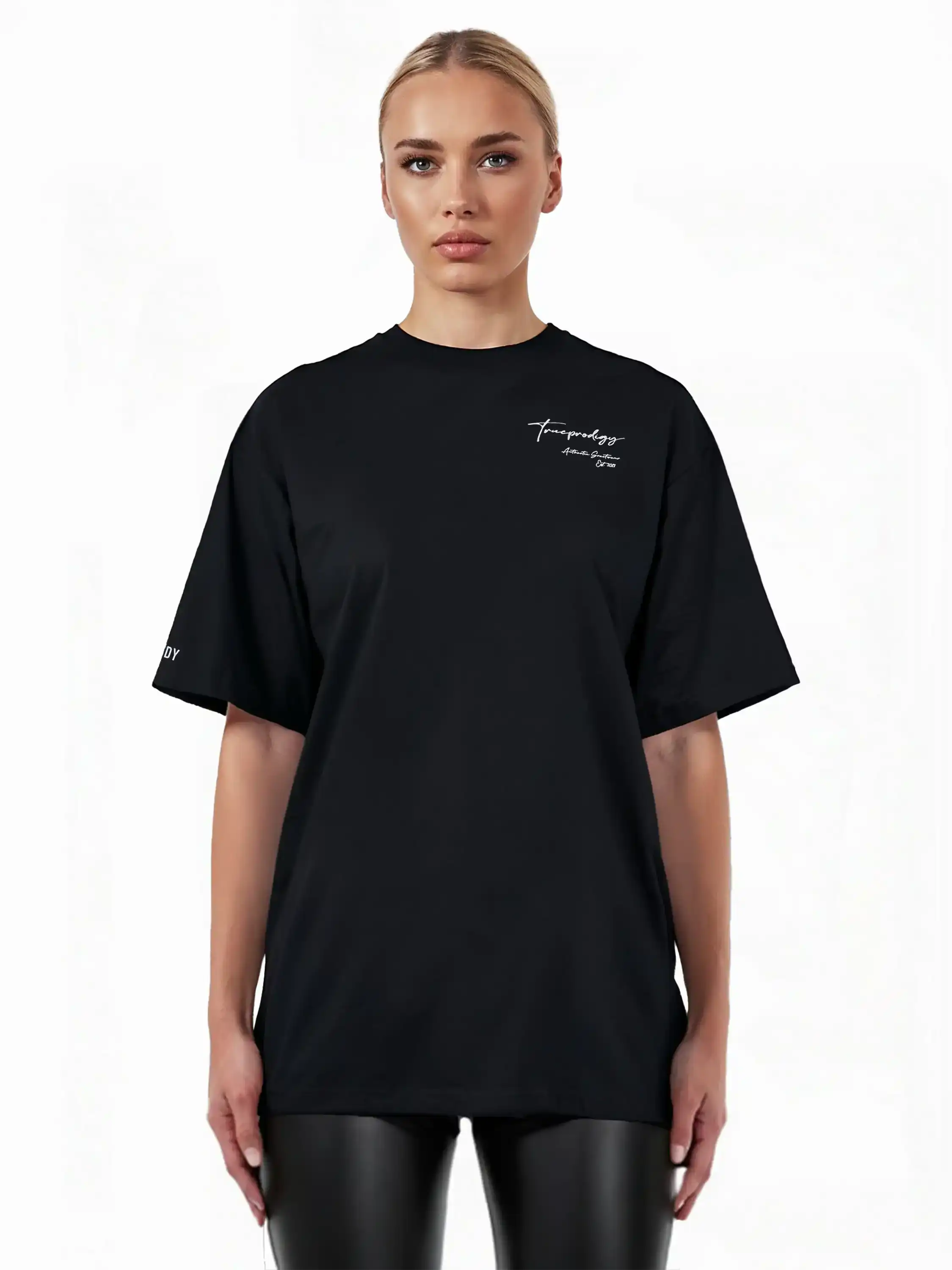 Eine Person mit zurückgesteckten blonden Haaren trägt das trueprodigy Marin F Oversize-T-Shirt mit feiner Logo-Schrift & TPDY-Print am Ärmel, gepaart mit einer schwarzen Kunstlederhose, vor einem schlichten weißen Hintergrund.