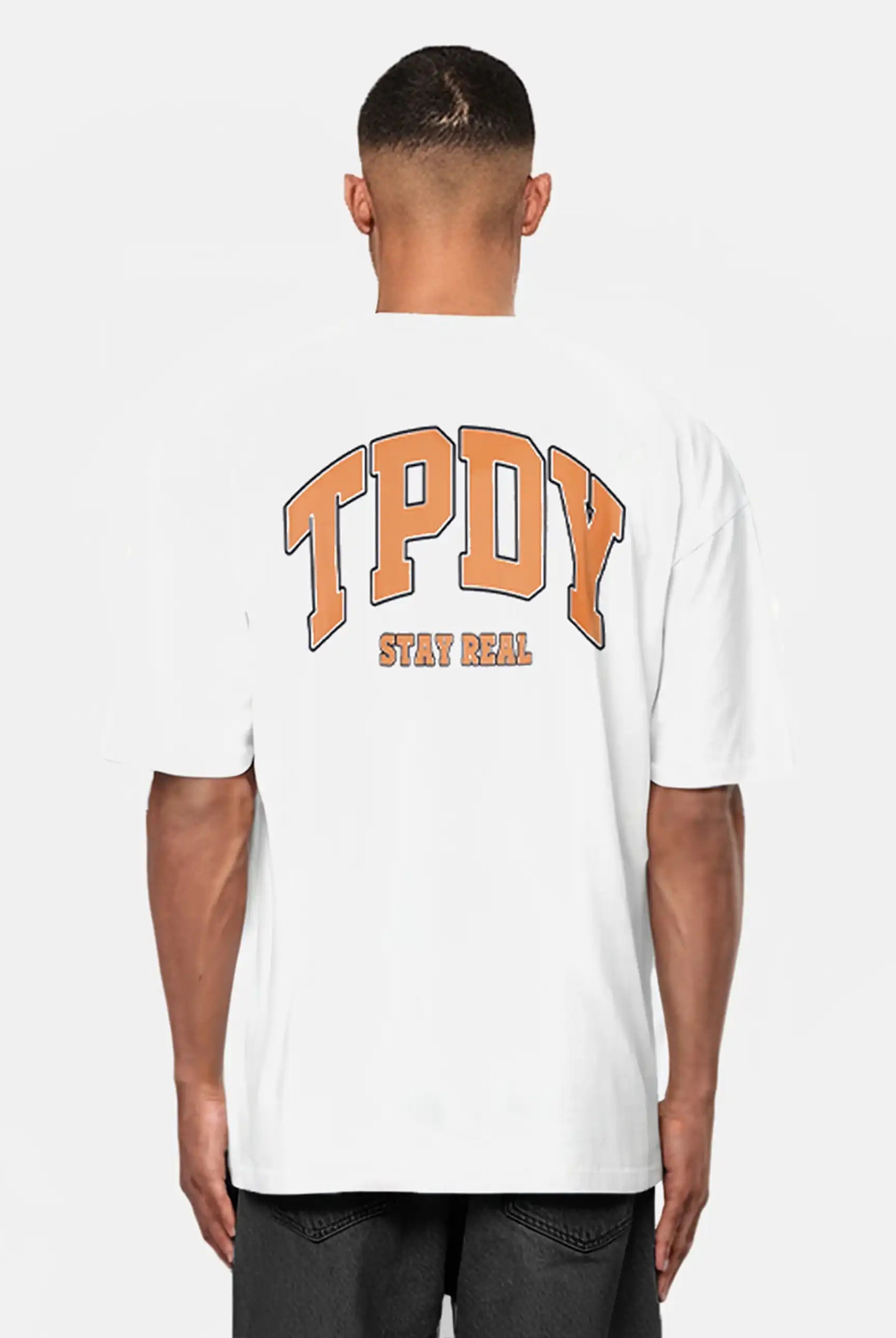 Jemand trägt das trueprodigy Oversize-Shirt mit TPDY-Logo & Rückenprint "Stay Real" - ein weißes Unisex-T-Shirt aus schwerem Jerseystoff mit auffälligem orangefarbenem TPDY-Schriftzug und "STAY REAL" am Rücken, vor hellem Hintergrund.