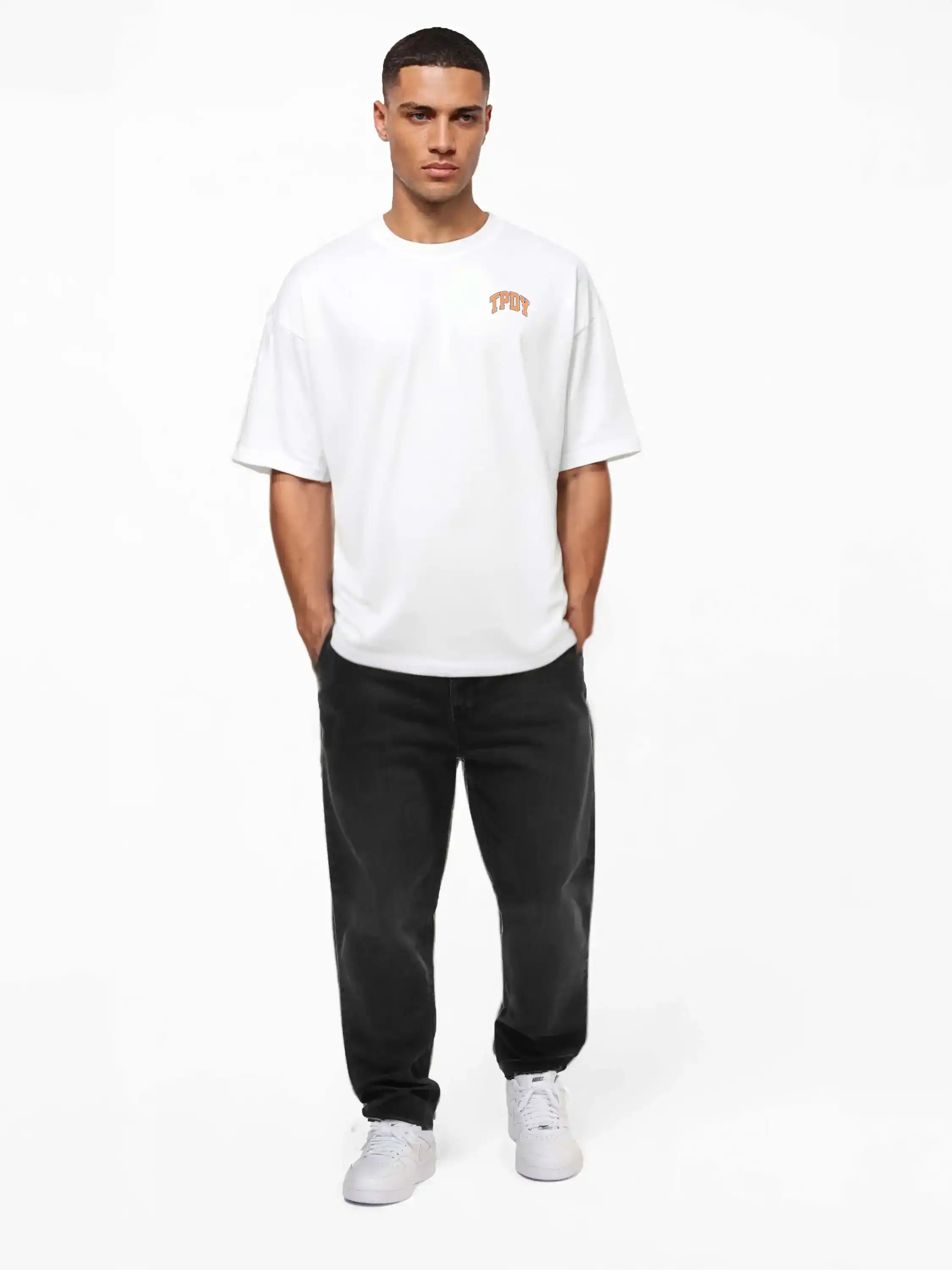 Ein Mann blickt nach vorne und trägt das trueprodigy Arin Oversize-Shirt mit TPDY-Logo & Rückenprint "Stay Real", gestylt mit schwarzen Jeans und weißen Turnschuhen, vor einem schlichten weißen Hintergrund.