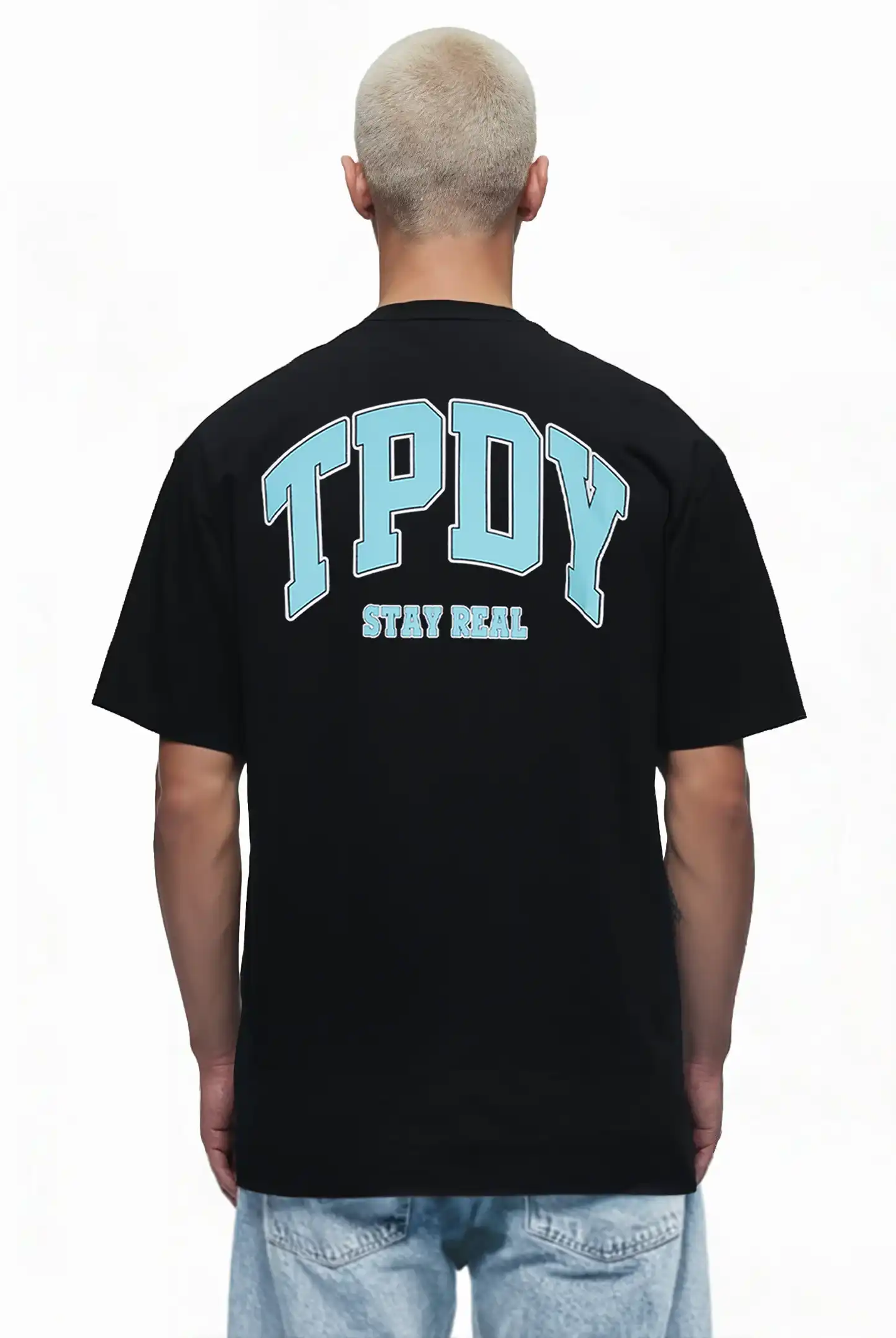 Eine Person mit kurzen, gebleichten Haaren ist von hinten zu sehen, die das trueprodigy Oversize-Shirt mit TPDY-Logo & Rückenprint "Stay Real" in Schwarz trägt, gestylt mit hellblauen Jeans.