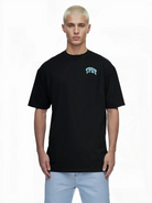 Eine Person mit kurzen, gebleichten blonden Haaren trägt das trueprodigy Arin Oversize-Shirt mit TPDY-Logo & Rückenprint "Stay Real" gepaart mit hellblauen Jeans, stehend vor einem weißen Hintergrund.