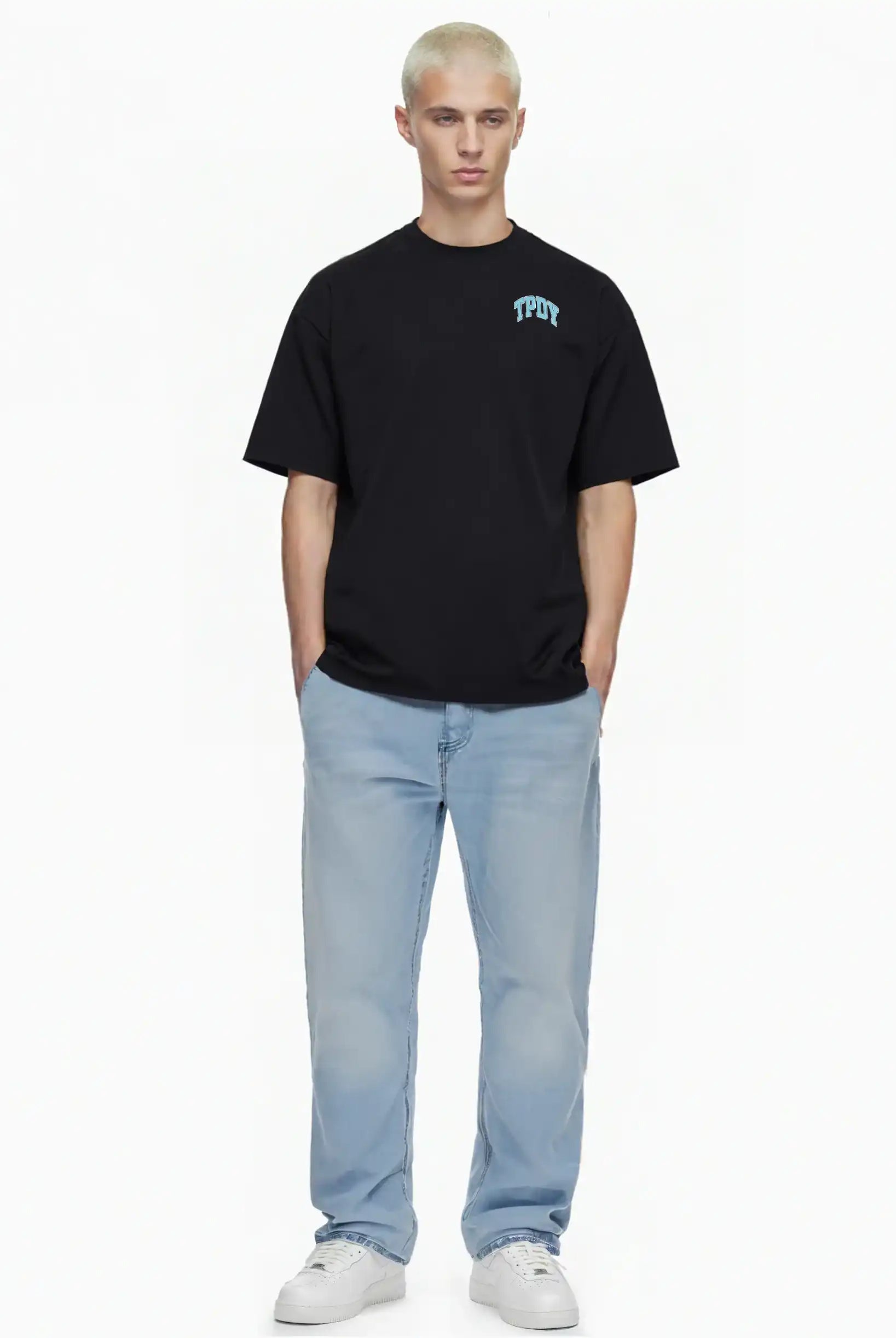 Eine Person mit kurzen, hellblonden Haaren steht vor einem weißen Hintergrund und trägt das trueprodigy Oversize-Shirt mit TPDY-Logo & Rückenprint "Stay Real", hellblaue Jeans und weiße Turnschuhe. Ihre Hände stecken in den Taschen.