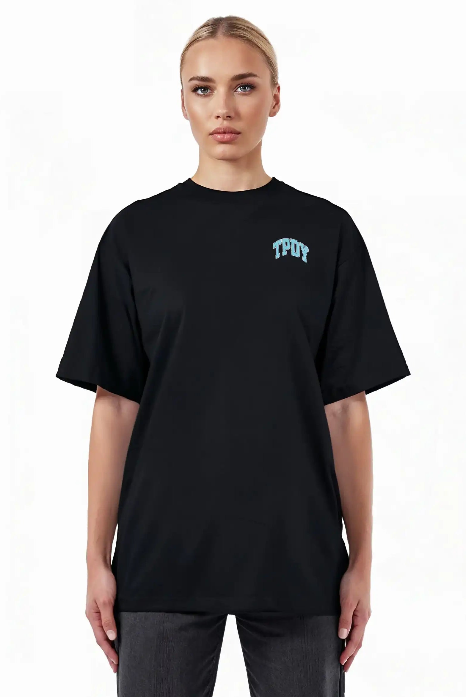 Eine blonde Person trägt das trueprodigy Arin F Oversize-T-Shirt aus dickem Jersey mit hellblauem TPDY-Print auf der linken Brust, steht vor weißem Hintergrund und zeigt das "Stay Real" Rückenmotiv.