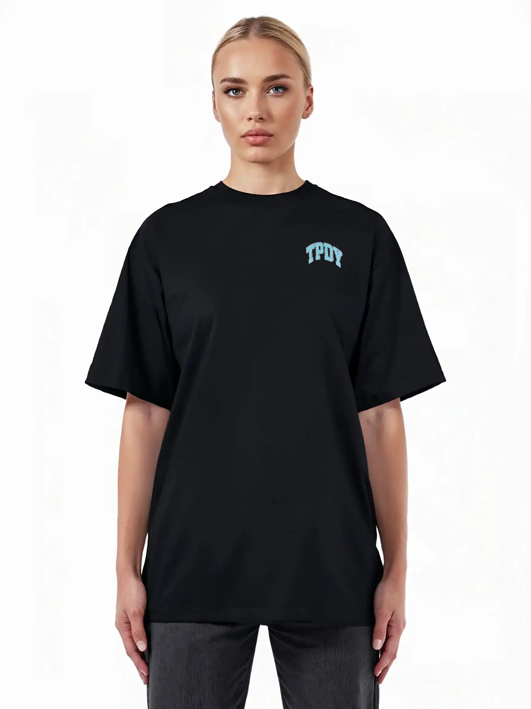 Eine blonde Person trägt das trueprodigy Arin F Oversize-T-Shirt aus dickem Jersey mit hellblauem TPDY-Print auf der linken Brust, steht vor weißem Hintergrund und zeigt das "Stay Real" Rückenmotiv.