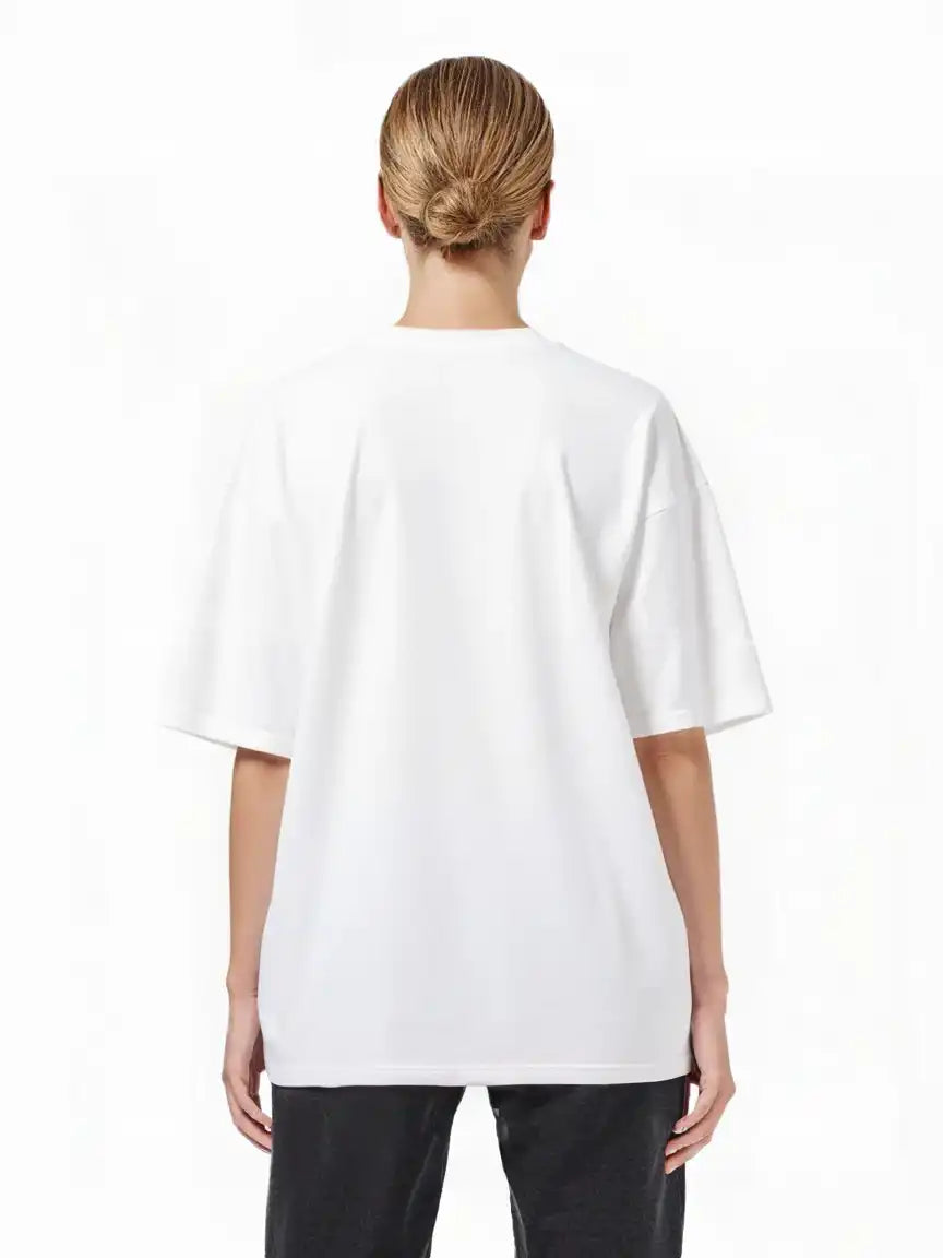 Eine Person mit hellbraunen Haaren in einem tiefen Dutt ist von hinten zu sehen. Sie trägt das trueprodigy Toni F Oversize-T-Shirt mit 3D-Schriftzug "TRUEPRODIGY" & "Rise Above Limits" und eine schwarze Hose vor einem schlichten weißen Hintergrund.