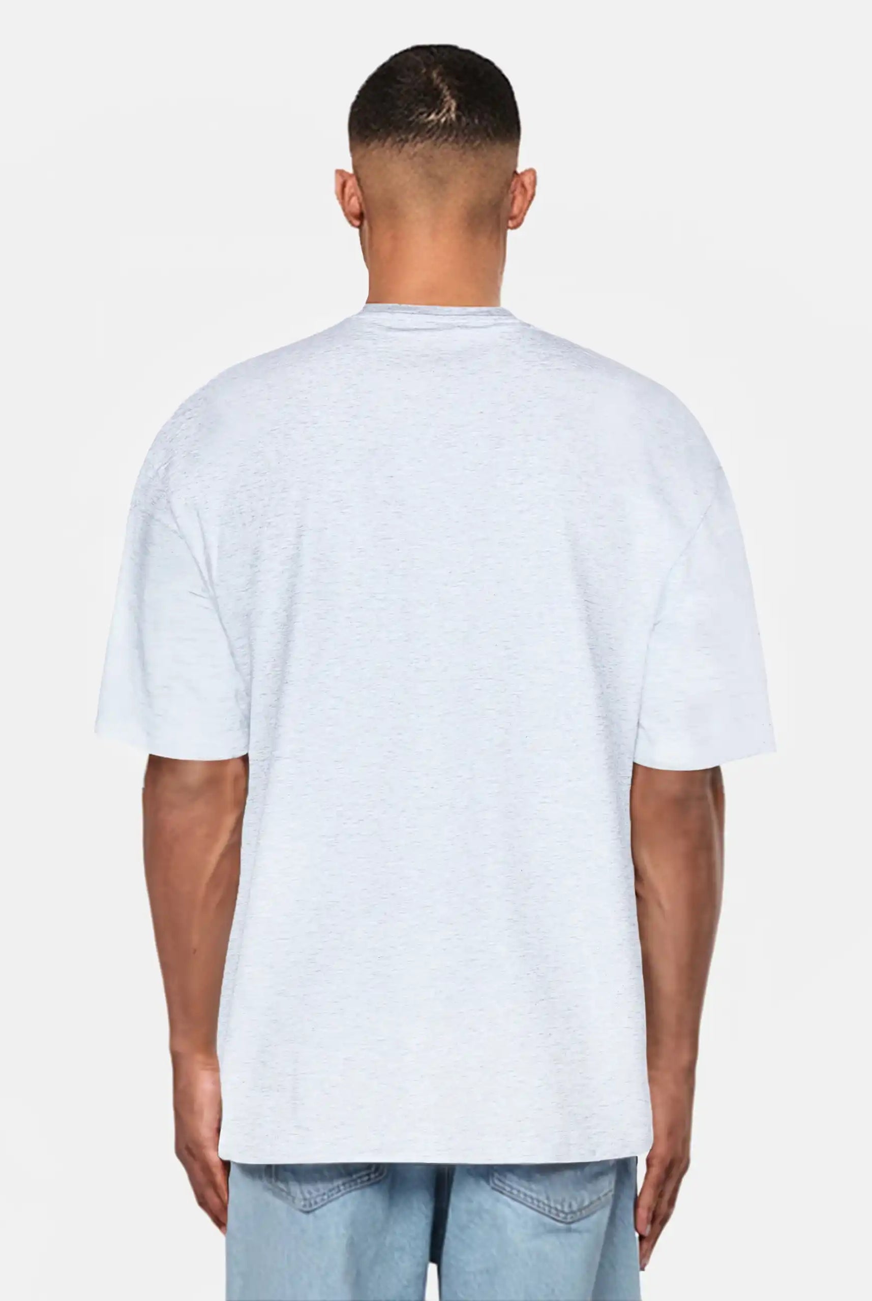 Ein Mann steht mit dem Rücken zur Kamera, trägt ein hellgraues trueprodigy Oversize-Herren-T-Shirt mit Logo-Smile-Grafik auf der Brust und hellblaue Denim-Shorts vor einem schlichten weißen Hintergrund.