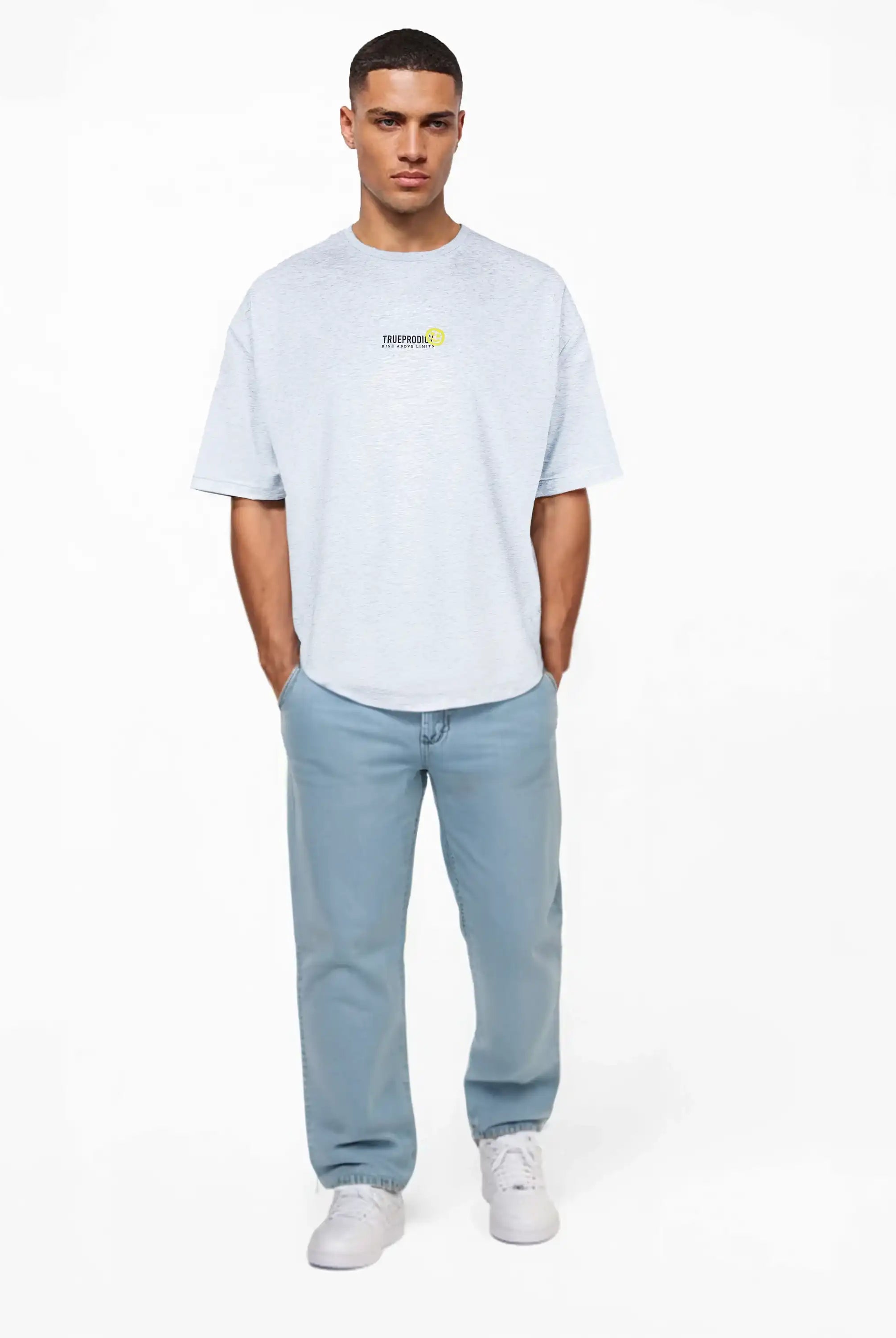 Ein Mann steht vor einem weißen Hintergrund, trägt ein hellgraues trueprodigy Oversize-Herren-T-Shirt mit Logo-Smile-Grafik auf der Brust, dazu hellblaue Jeans und weiße Turnschuhe, die Hände lässig in den Taschen.