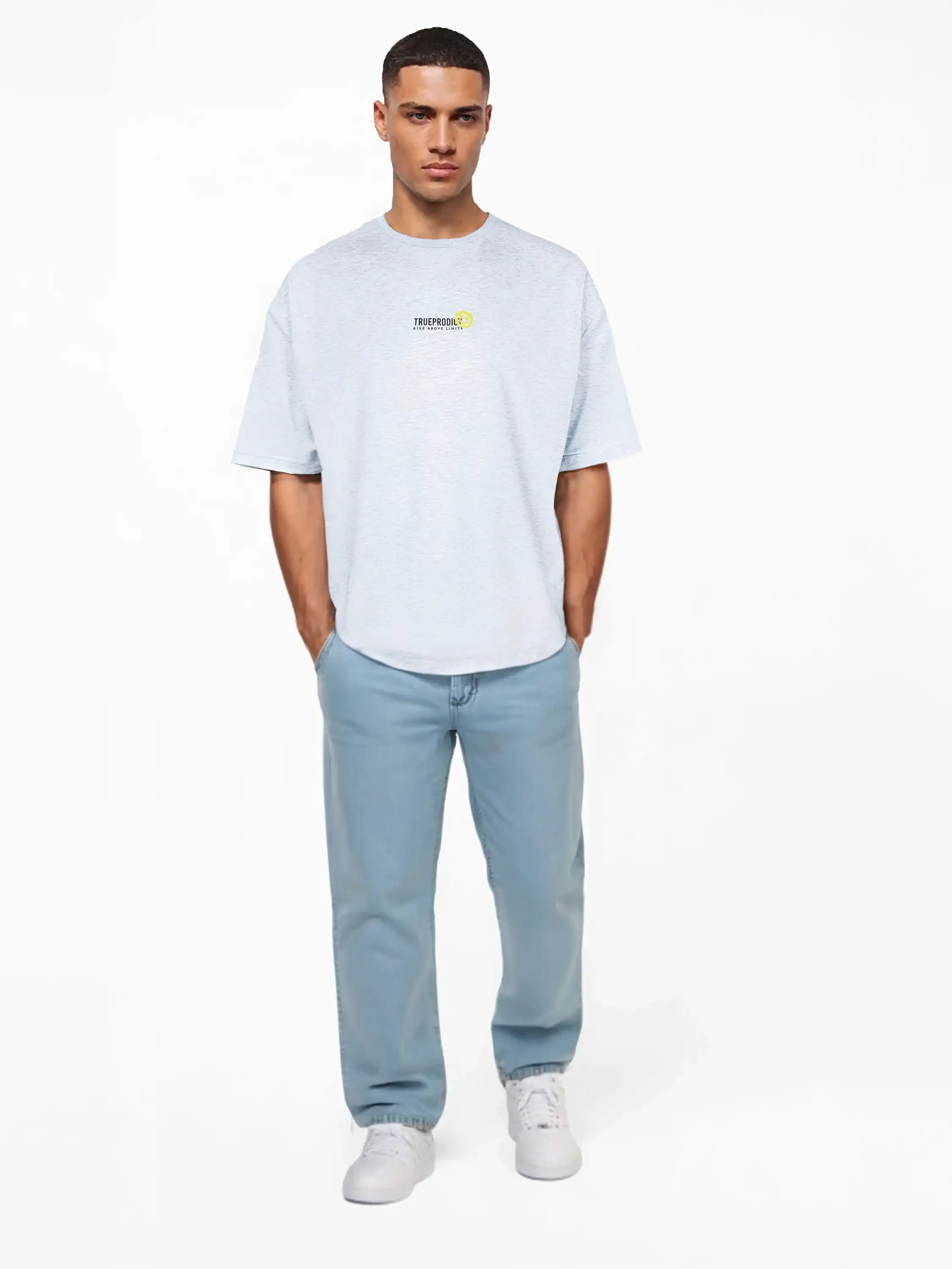 Ein Mann steht vor einem weißen Hintergrund, trägt ein hellgraues trueprodigy Oversize-Herren-T-Shirt mit Logo-Smile-Grafik auf der Brust, dazu hellblaue Jeans und weiße Turnschuhe, die Hände lässig in den Taschen.