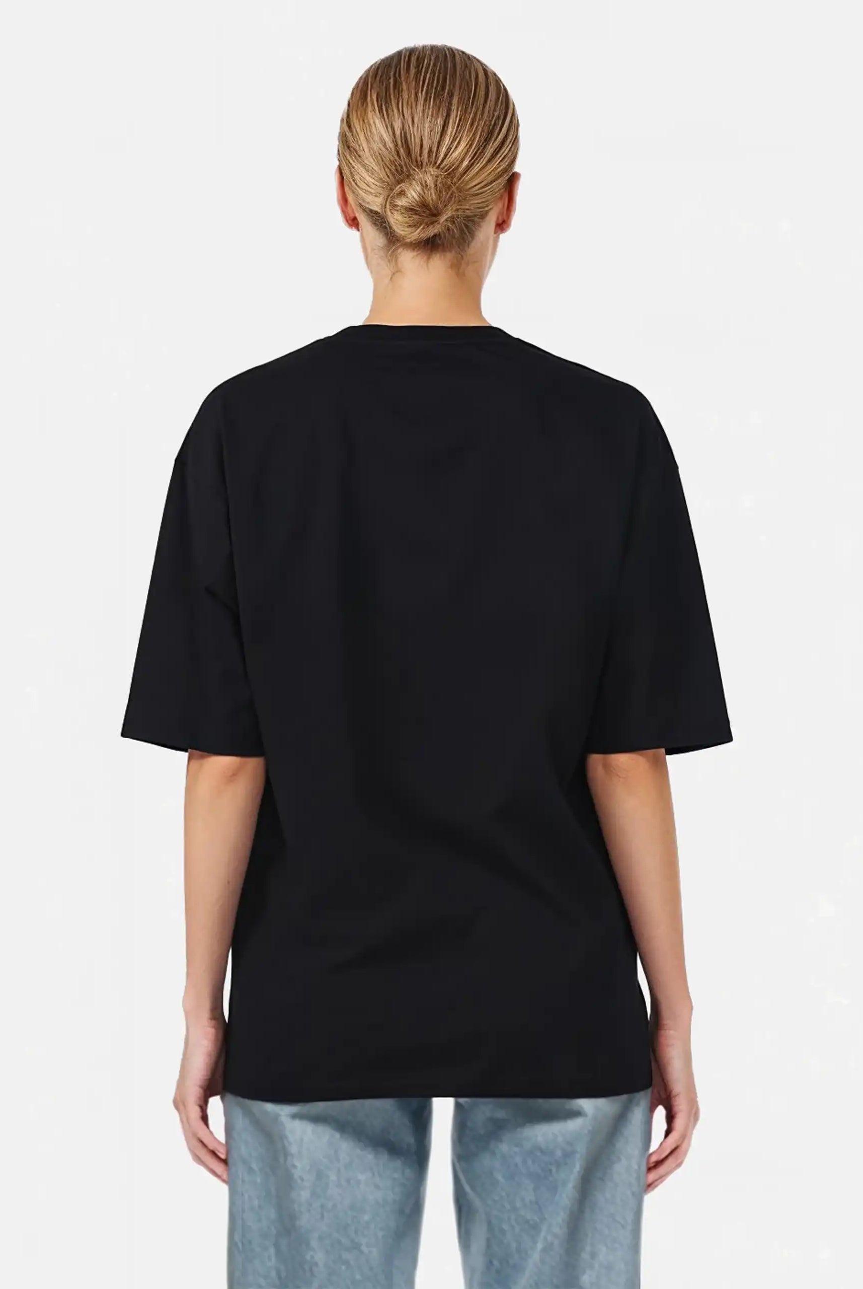 Gezeigt wird eine Person mit blondem Haar in einem tiefen Dutt von hinten, die ein trueprodigy Juniper F Oversize-Damen-T-Shirt mit Logo-Smile-Grafik auf der Vorderseite und hellblaue Jeans vor einem schlichten weißen Hintergrund trägt.