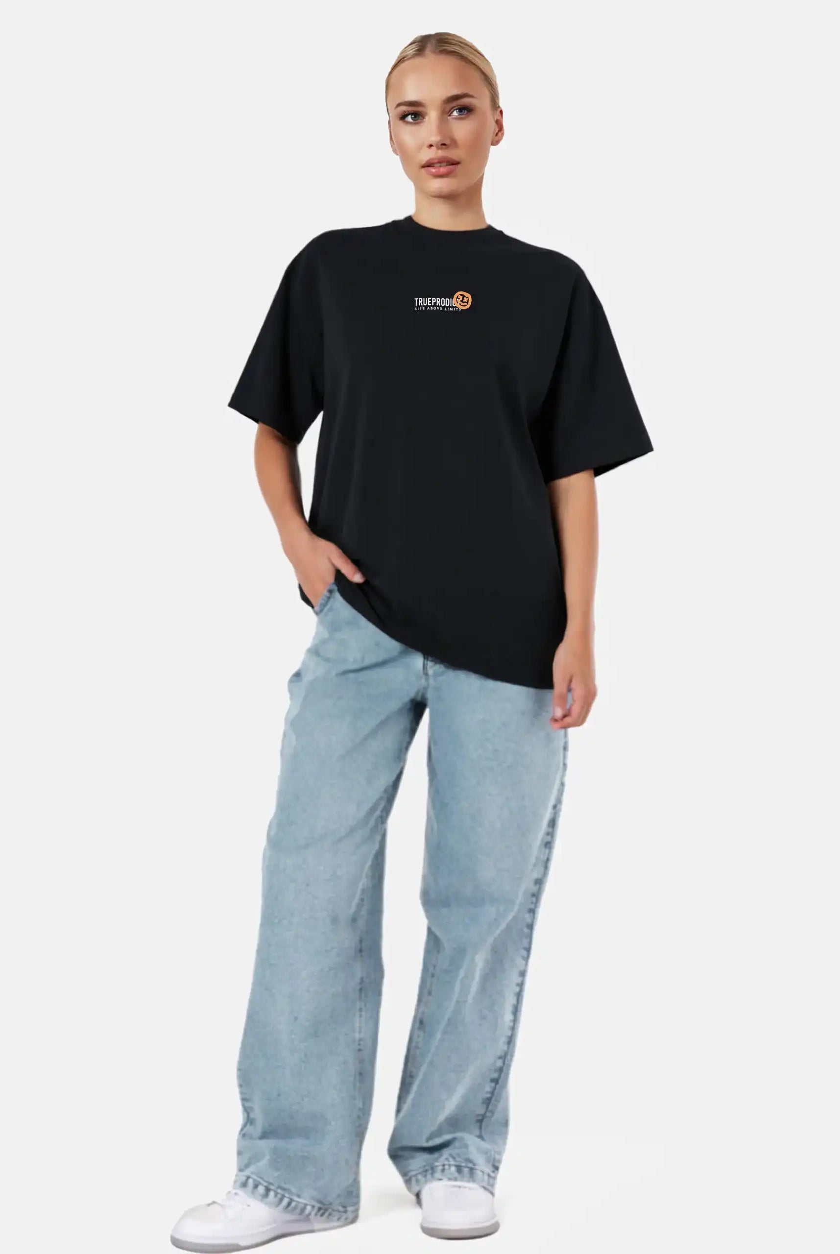 Vor einem schlichten weißen Hintergrund trägt eine Person das trueprodigy Juniper F Oversize-Damen-T-Shirt mit Logo-Smile-Grafik auf der Vorderseite in Schwarz, gepaart mit hellblauen Röhrenjeans und weißen Sneakers.