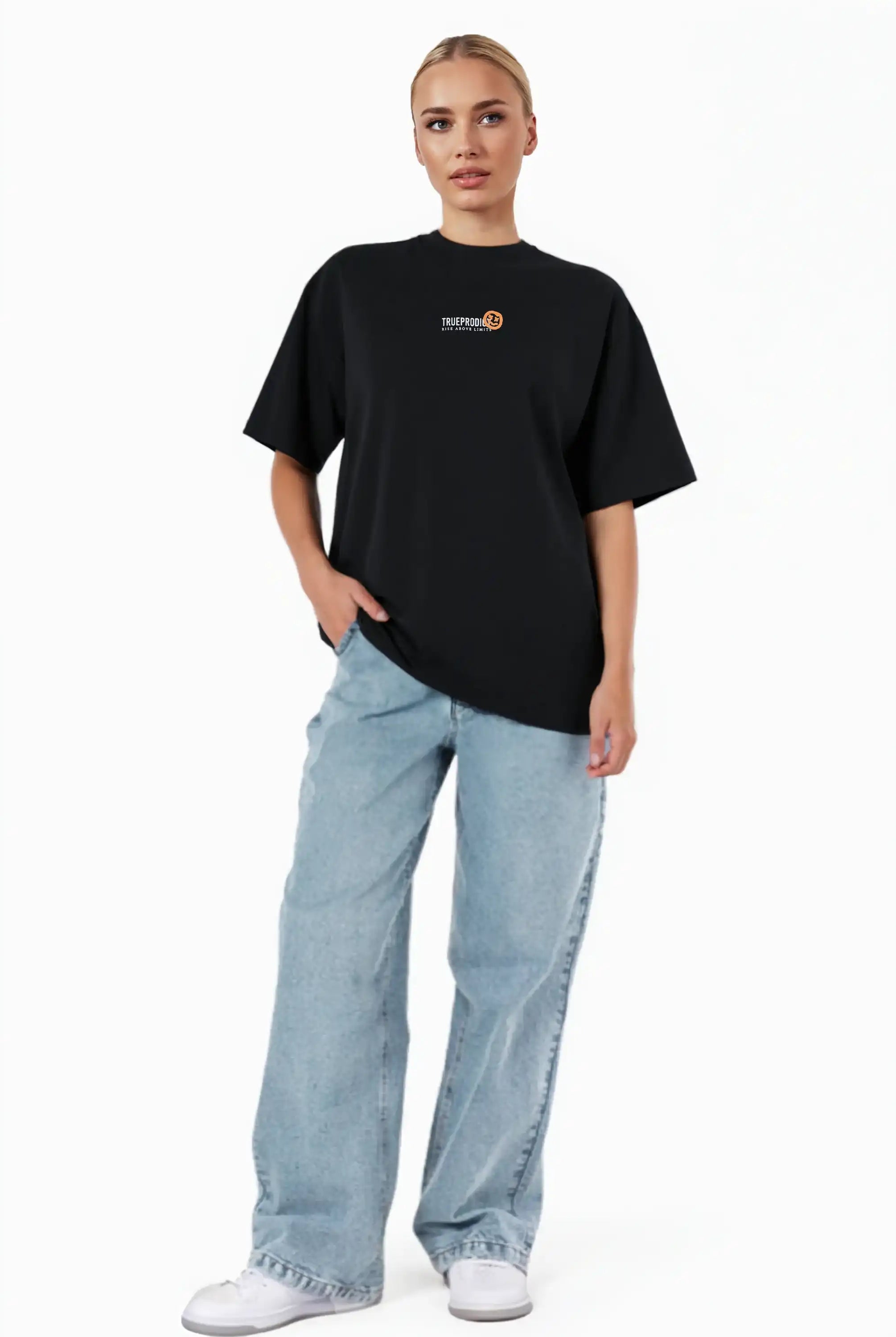 Eine Person steht vor einem weißen Hintergrund und trägt das trueprodigy Juniper F Oversize-Damen-T-Shirt mit Logo-Smile-Grafik auf der Vorderseite, hellblaue Baggy Jeans und weiße Turnschuhe. Eine Hand steckt in der Tasche.