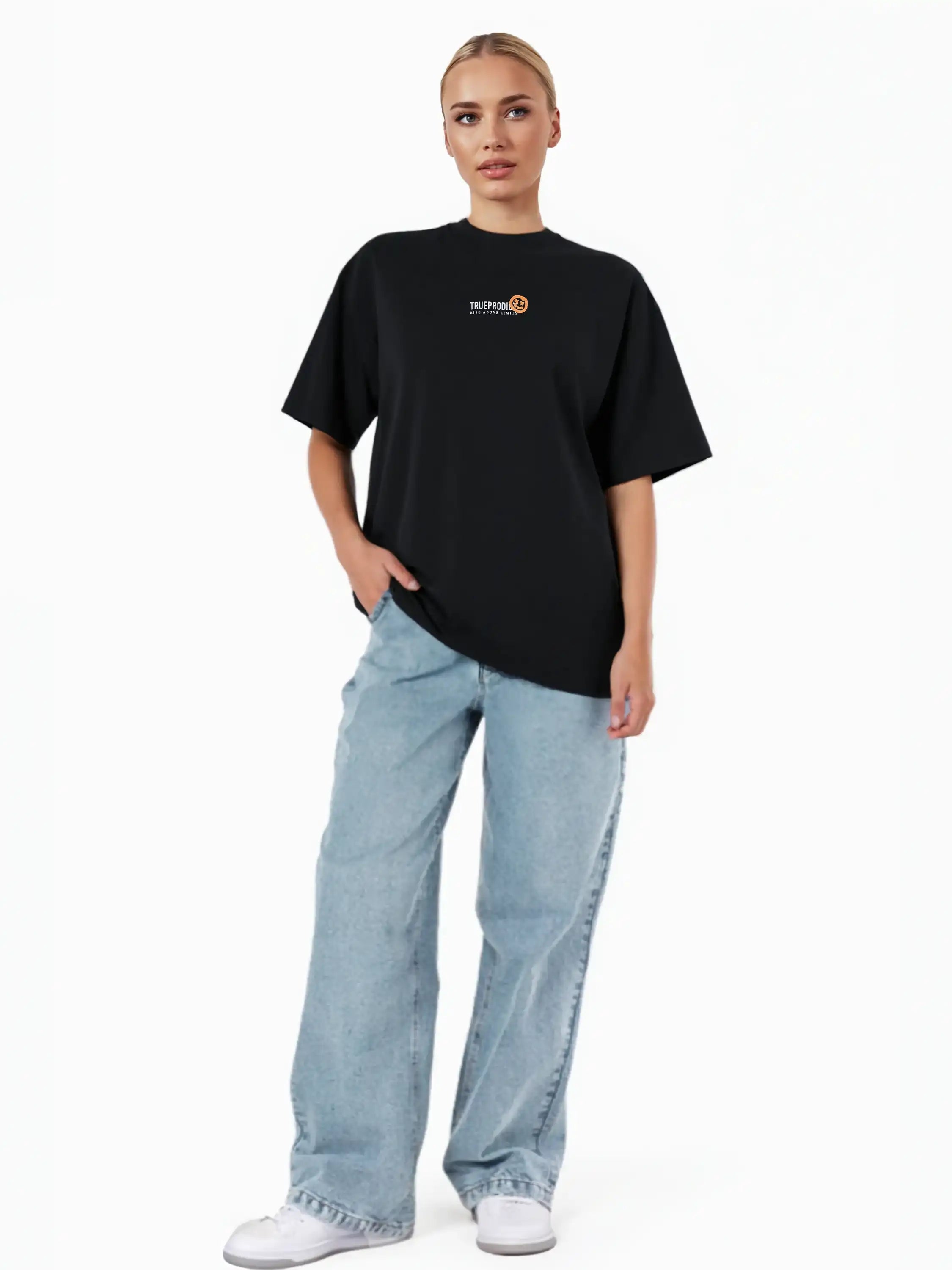 Eine Person steht vor einem weißen Hintergrund und trägt das trueprodigy Juniper F Oversize-Damen-T-Shirt mit Logo-Smile-Grafik auf der Vorderseite, hellblaue Baggy Jeans und weiße Turnschuhe. Eine Hand steckt in der Tasche.