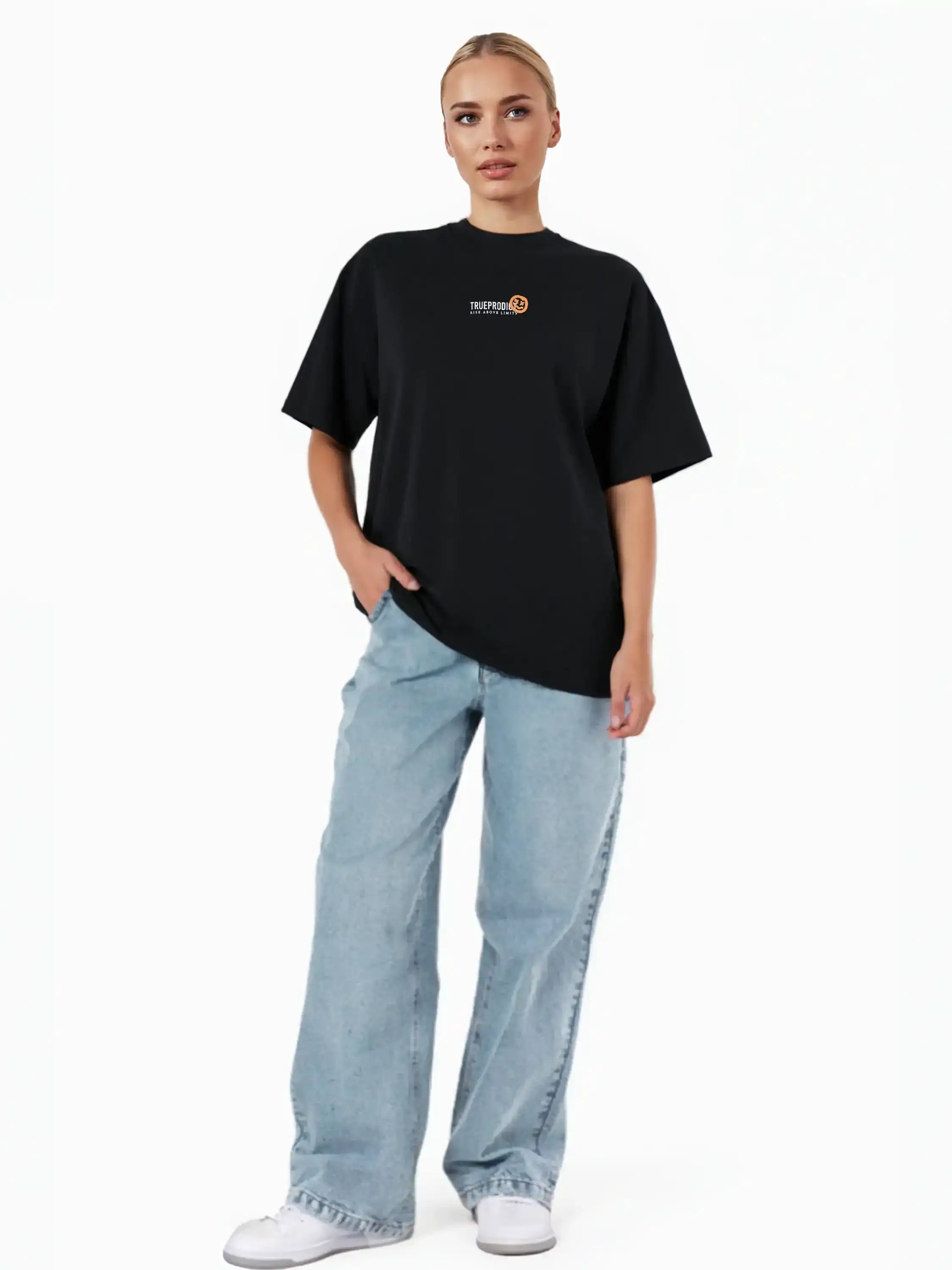 Eine Person steht vor einem weißen Hintergrund und trägt das trueprodigy Juniper F Oversize-Damen-T-Shirt mit Logo-Smile-Grafik auf der Vorderseite, hellblaue Baggy Jeans und weiße Turnschuhe. Eine Hand steckt in der Tasche.