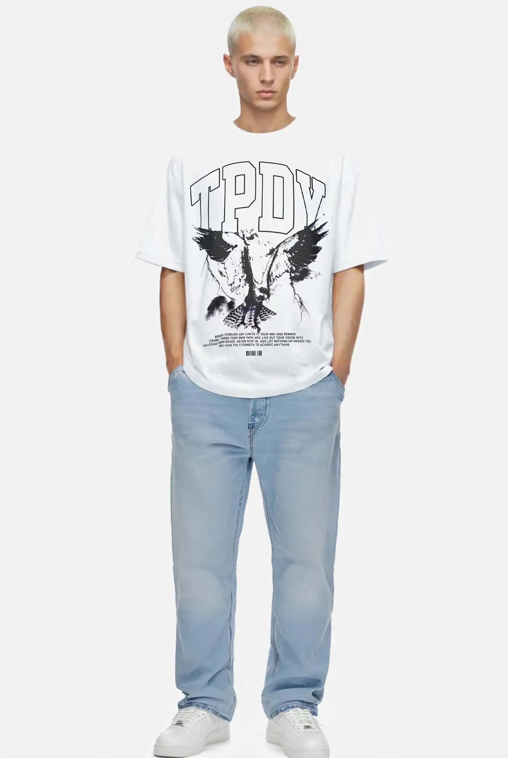 Eine Person mit kurzen gebleichten Haaren trägt das trueprodigy Yuki Oversize-T-Shirt mit Adlergrafik & TPDY-Schriftzug aus schwerem Jerseystoff, gepaart mit hellblauen Jeans und weißen Turnschuhen, vor einem schlichten weißen Hintergrund.