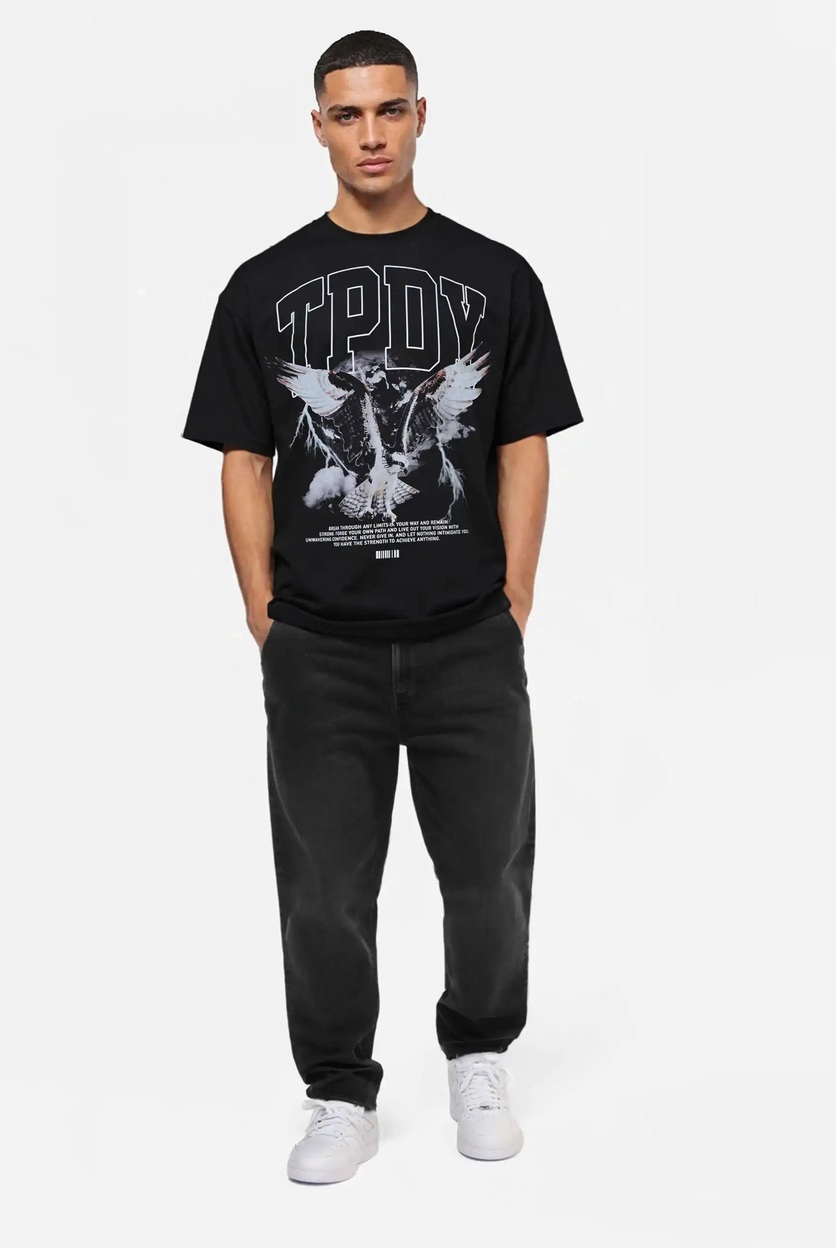 Eine Person steht vor einem weißen Hintergrund und trägt das trueprodigy Yuki Oversize-T-Shirt mit Adlergrafik & TPDY-Schriftzug in Schwarz, gepaart mit schwarzen Jeans und weißen Sneakers.