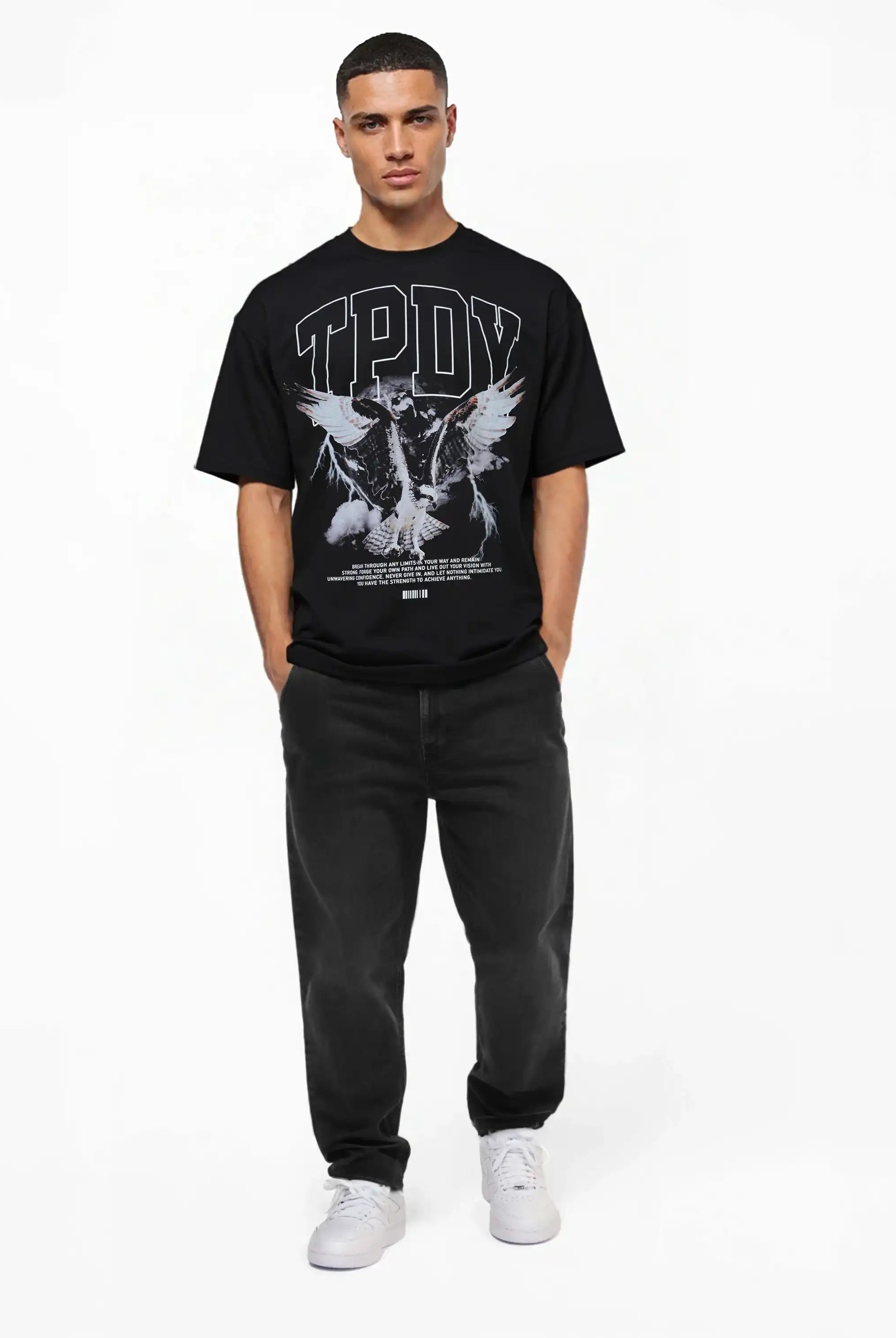 Ein Mann steht mit dem Gesicht nach vorne und trägt ein schwarzes trueprodigy Yuki Oversize-T-Shirt mit Adlergrafik & TPDY-Schriftzug, schwarze Jeans und weiße Turnschuhe vor einem schlichten weißen Hintergrund.