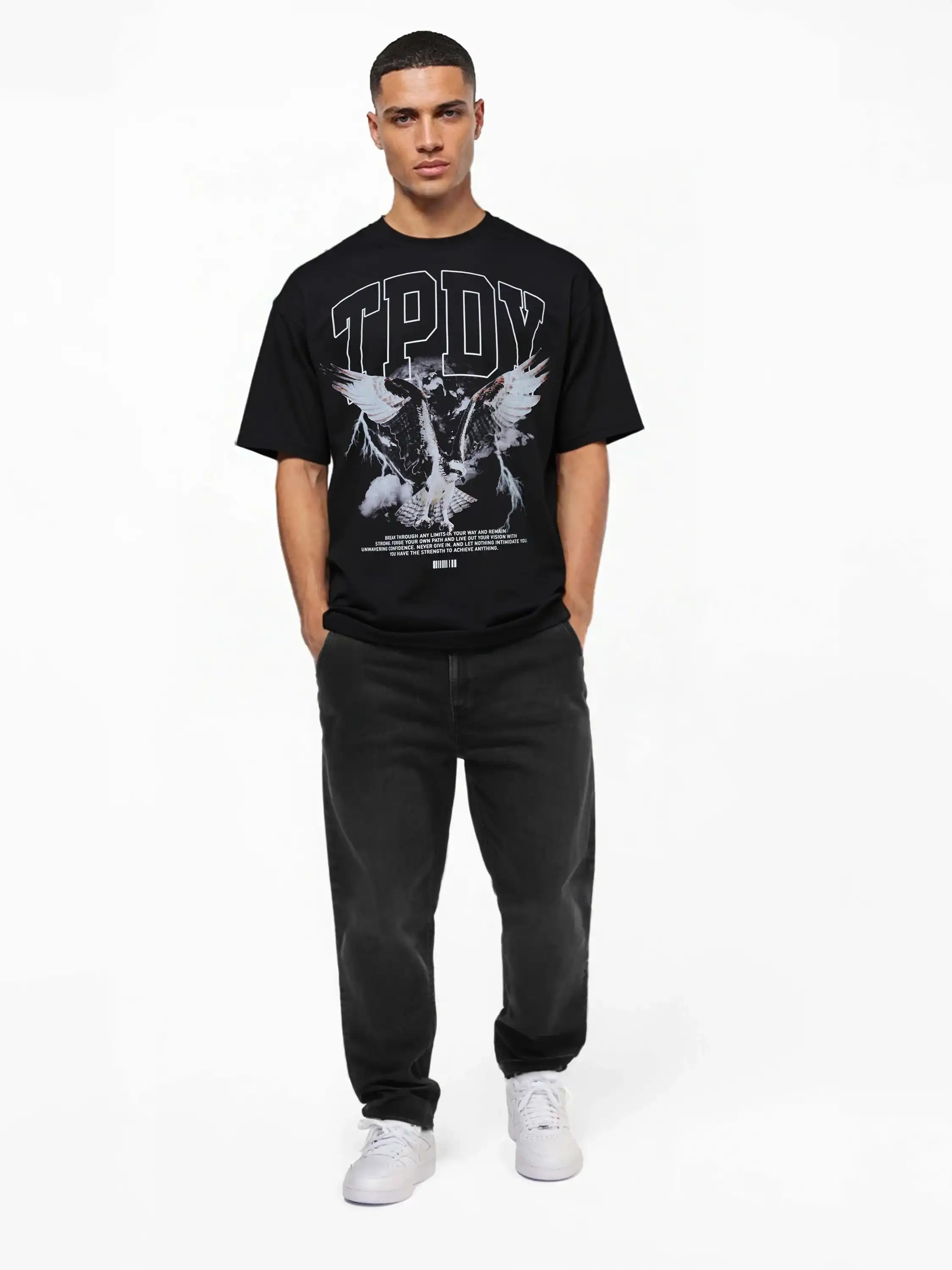 Ein Mann steht mit dem Gesicht nach vorne und trägt ein schwarzes trueprodigy Yuki Oversize-T-Shirt mit Adlergrafik & TPDY-Schriftzug, schwarze Jeans und weiße Turnschuhe vor einem schlichten weißen Hintergrund.