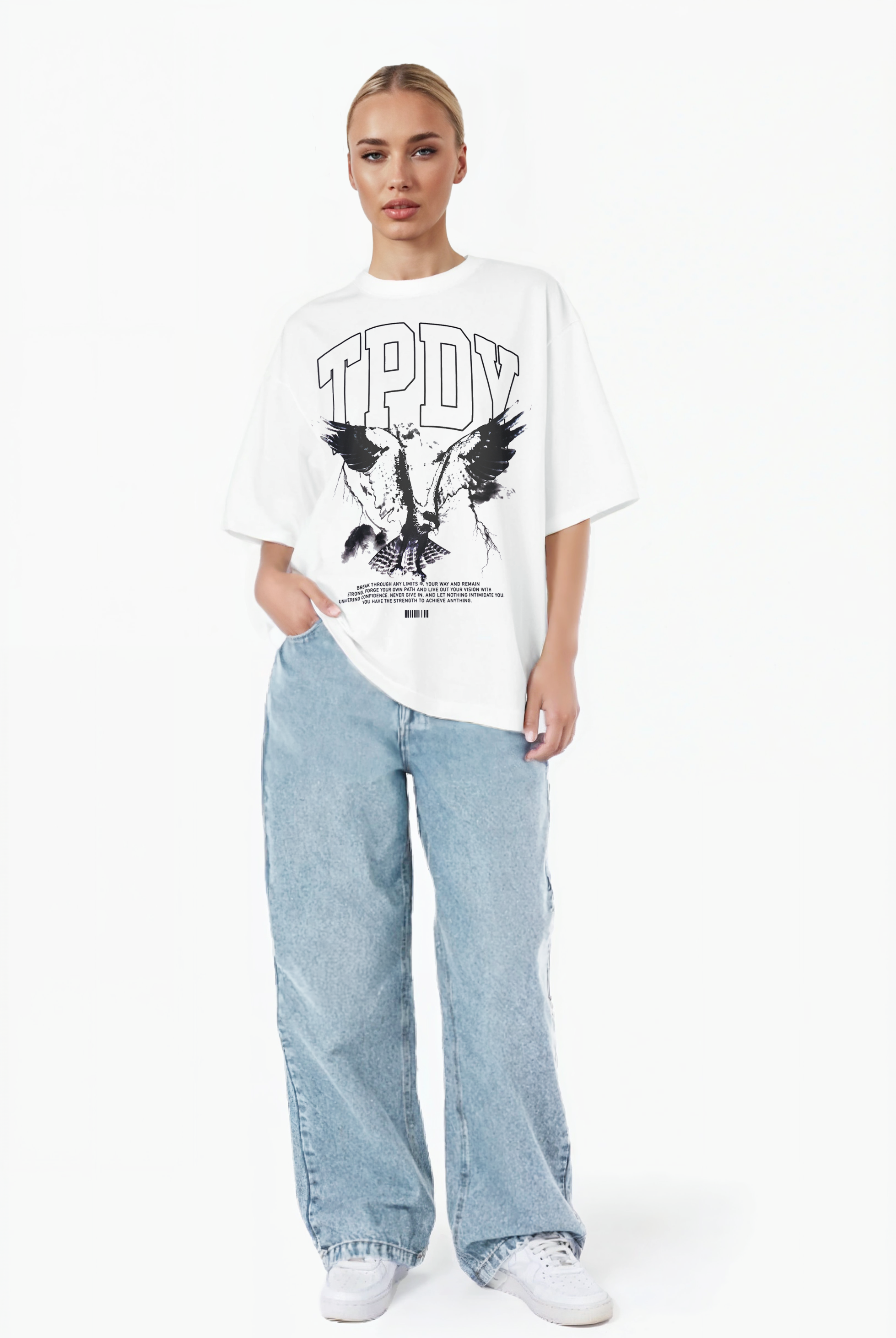 Eine Person steht vor einem weißen Hintergrund und trägt ein weißes trueprodigy Oversize-T-Shirt mit Adlergrafik & TRUEPRODIGY-Schriftzug, lockere hellblaue Jeans und weiße Turnschuhe. Eine Hand steckt in ihrer Tasche.