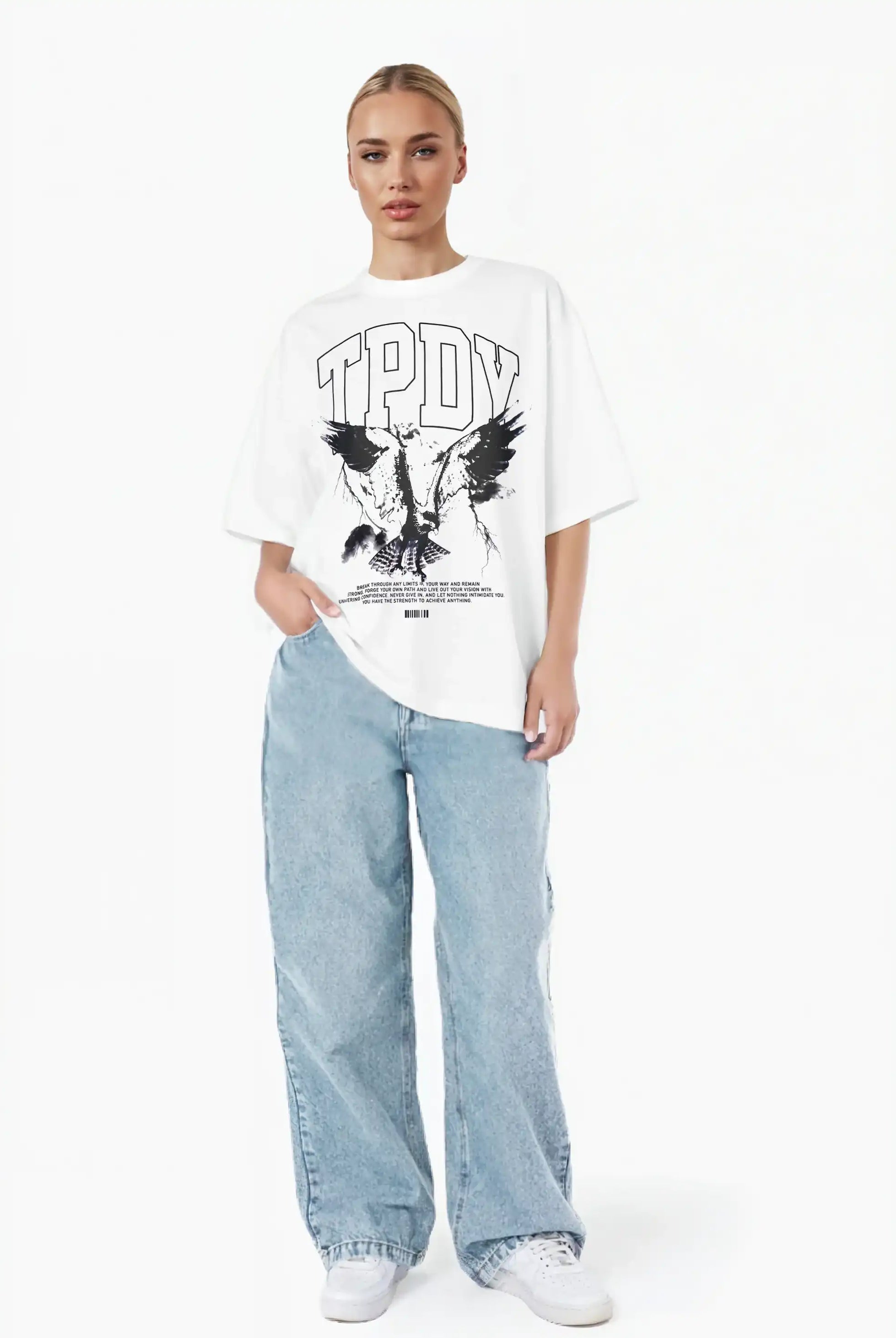 Eine Person steht vor einem weißen Hintergrund und trägt ein weißes trueprodigy Oversize-T-Shirt mit Adlergrafik & TRUEPRODIGY-Schriftzug, lockere hellblaue Jeans und weiße Turnschuhe. Eine Hand steckt in ihrer Tasche.