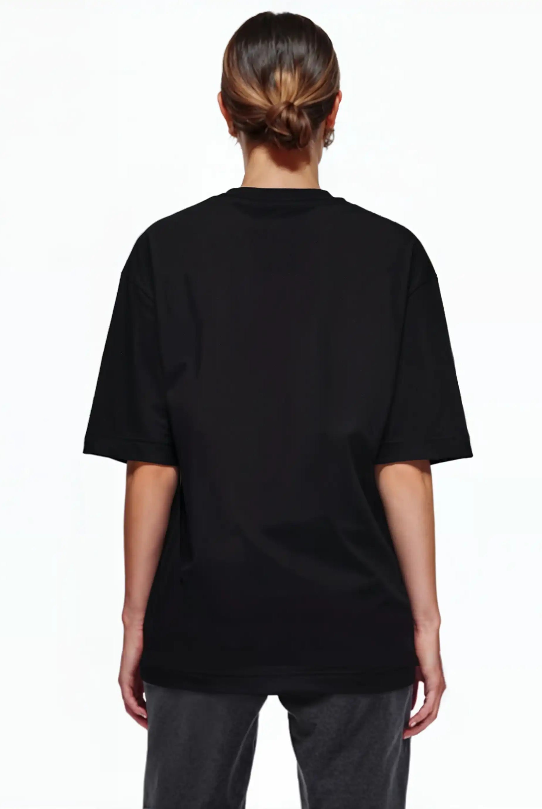 Eine Person mit braunen Haaren in einem tiefen Dutt ist von hinten zu sehen. Sie trägt ein trueprodigy Oversize-T-Shirt mit Adlergrafik & TRUEPRODIGY-Schriftzug und eine dunkle Hose und steht vor einem schlichten weißen Hintergrund.