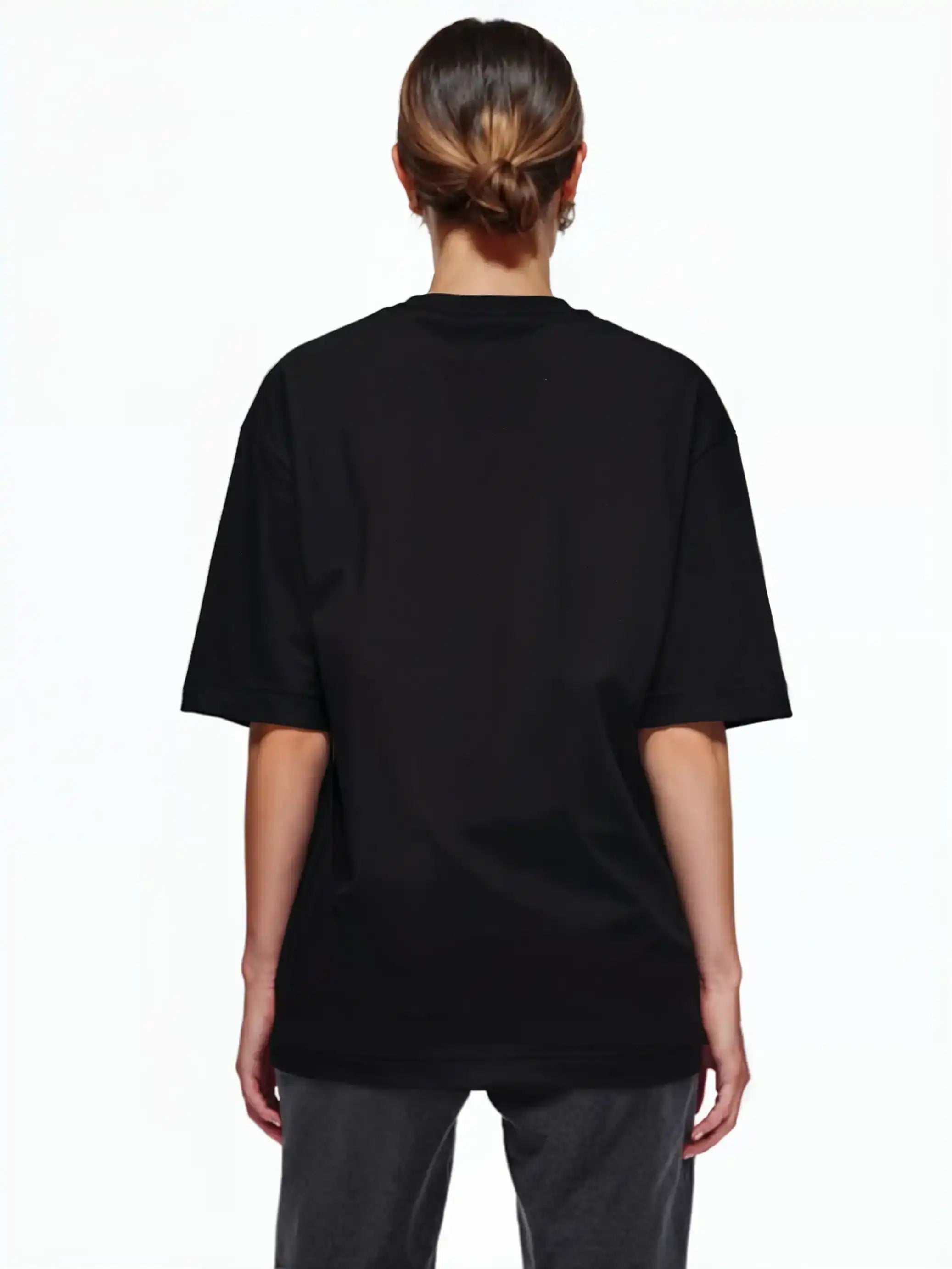 Eine Person mit braunen Haaren in einem tiefen Dutt ist von hinten zu sehen. Sie trägt ein trueprodigy Oversize-T-Shirt mit Adlergrafik & TRUEPRODIGY-Schriftzug und eine dunkle Hose und steht vor einem schlichten weißen Hintergrund.