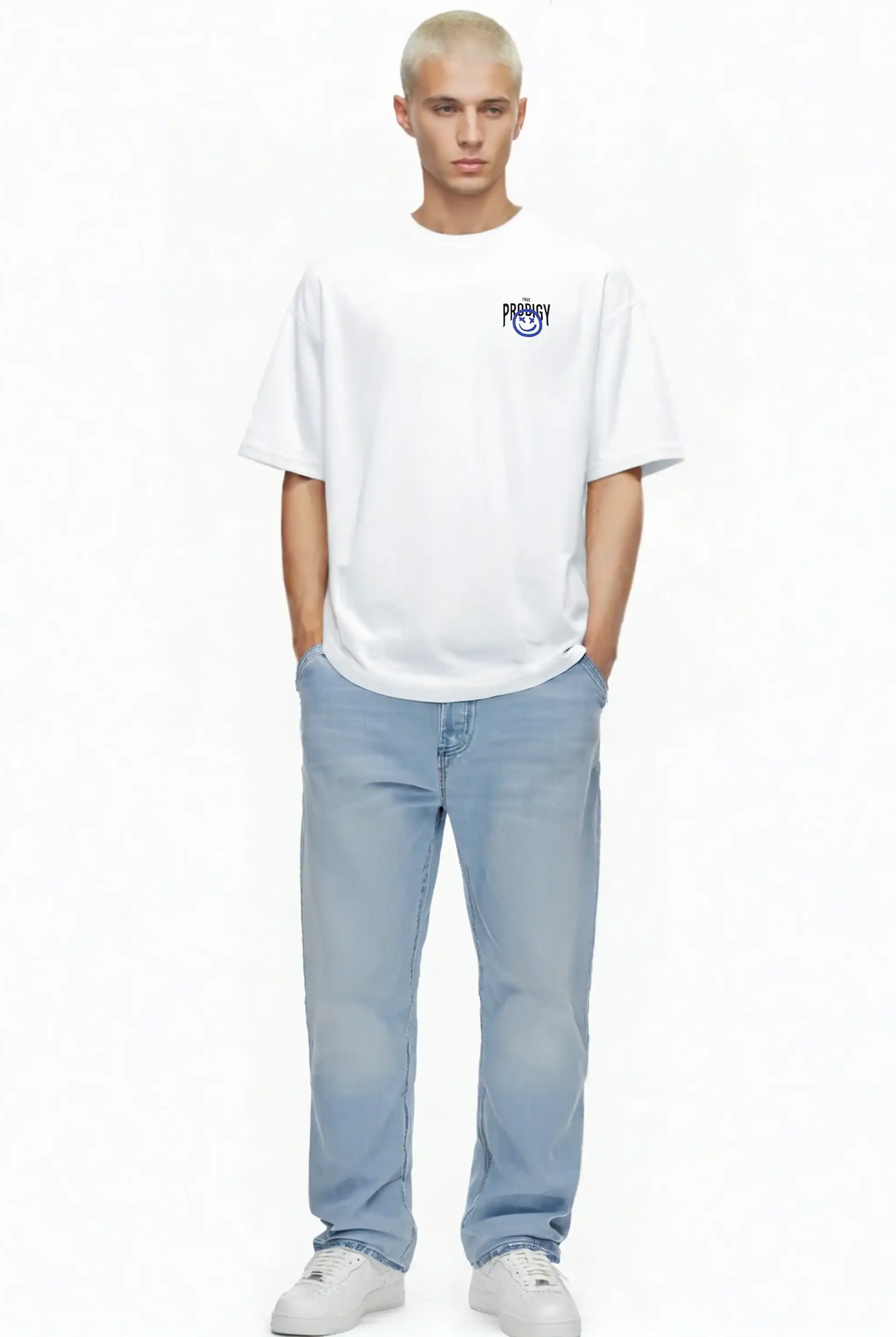 Eine Person mit kurzen blonden Haaren steht vor einem weißen Hintergrund und trägt das trueprodigy Hajin Oversize-T-Shirt mit Spray-Smiley & Rückenprint "Happy Mind", hellblaue Jeans und weiße Sneakers, die Hände lässig in den Taschen.