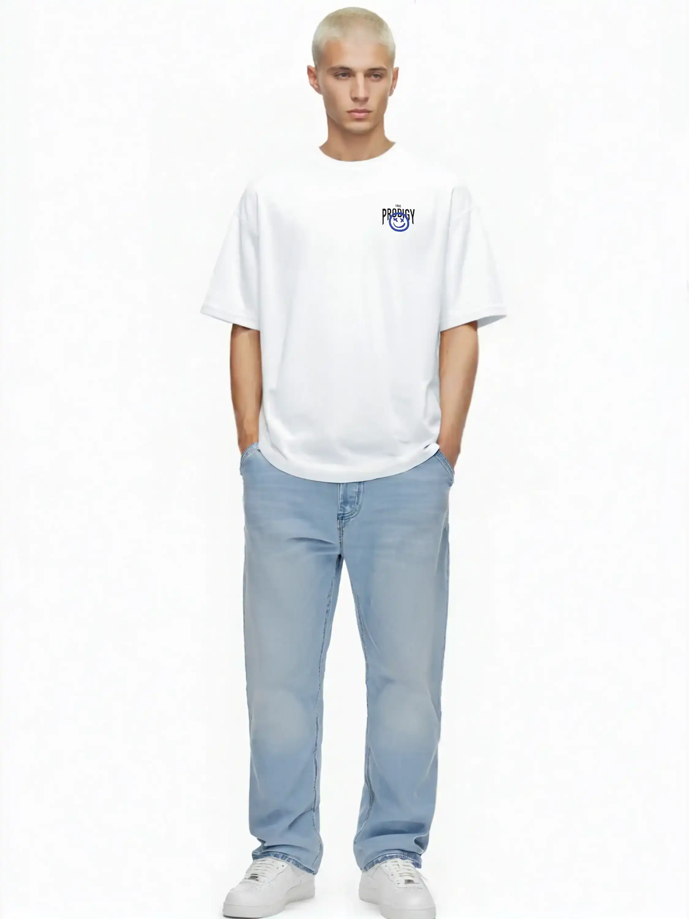 Eine Person mit kurzen blonden Haaren steht vor einem weißen Hintergrund und trägt das trueprodigy Hajin Oversize-T-Shirt mit Spray-Smiley & Rückenprint "Happy Mind", hellblaue Jeans und weiße Sneakers, die Hände lässig in den Taschen.