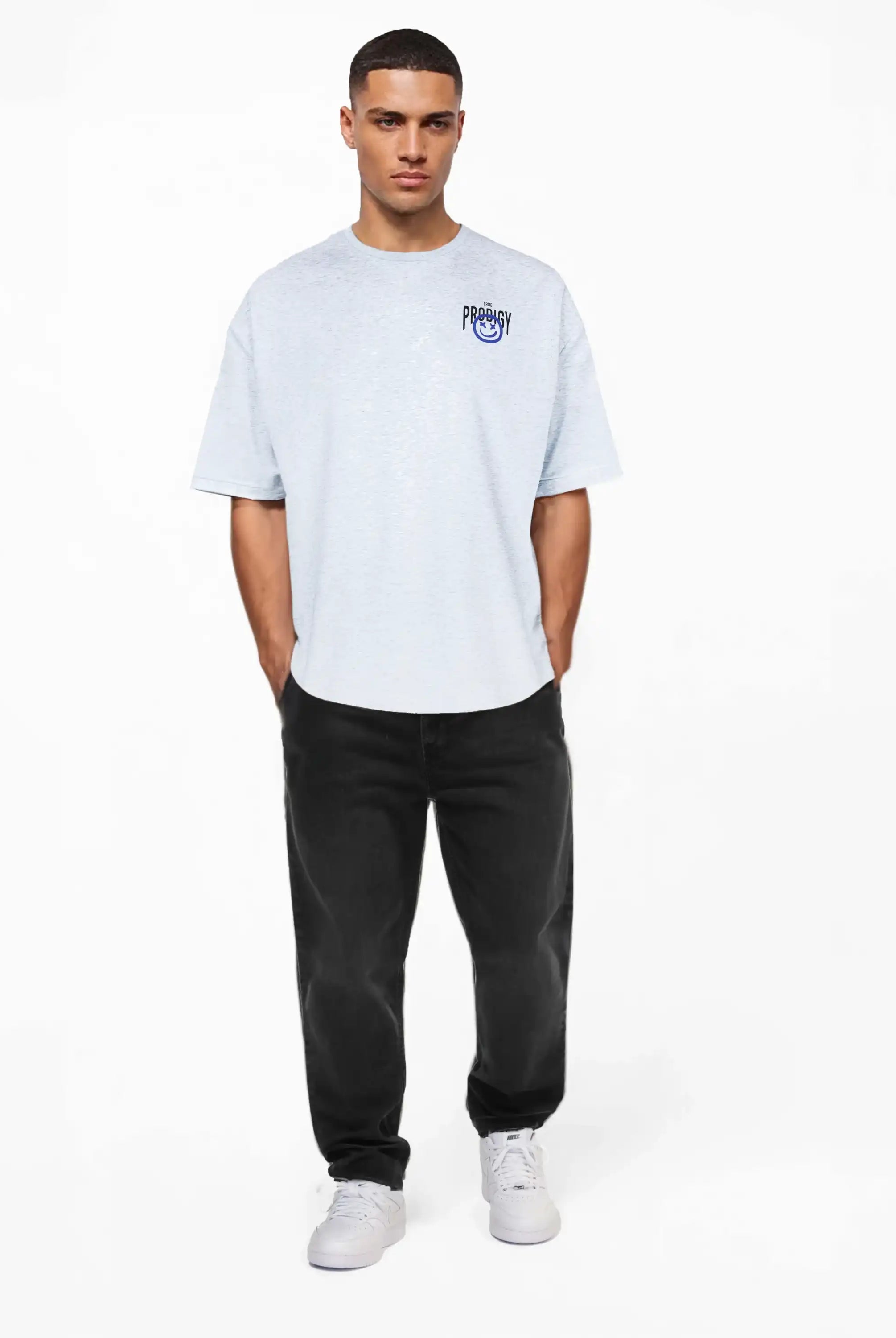 Ein Mann steht vor einem schlichten weißen Hintergrund und trägt das trueprodigy Oversize-T-Shirt mit Spray-Smiley & Rückenprint "Happy Mind" mit kleiner blauer Brustgrafik, gepaart mit schwarzer Jeans und weißen Turnschuhen, die Hände in den Taschen, den Blick nach vorne gerichtet.