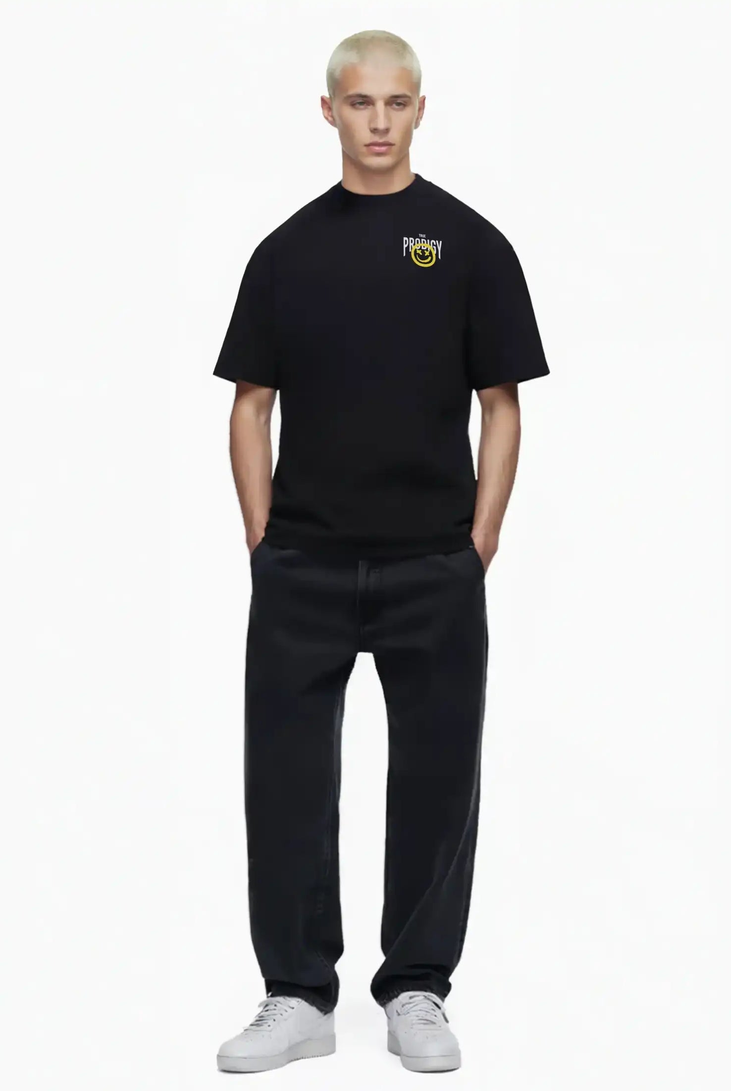 Eine Person mit kurzen blonden Haaren blickt nach vorne und trägt das trueprodigy Hajin Oversize-T-Shirt mit Spray-Smiley & Rückenprint "Happy Mind", gepaart mit schwarzen Jeans und weißen Turnschuhen, vor einem schlichten weißen Hintergrund.